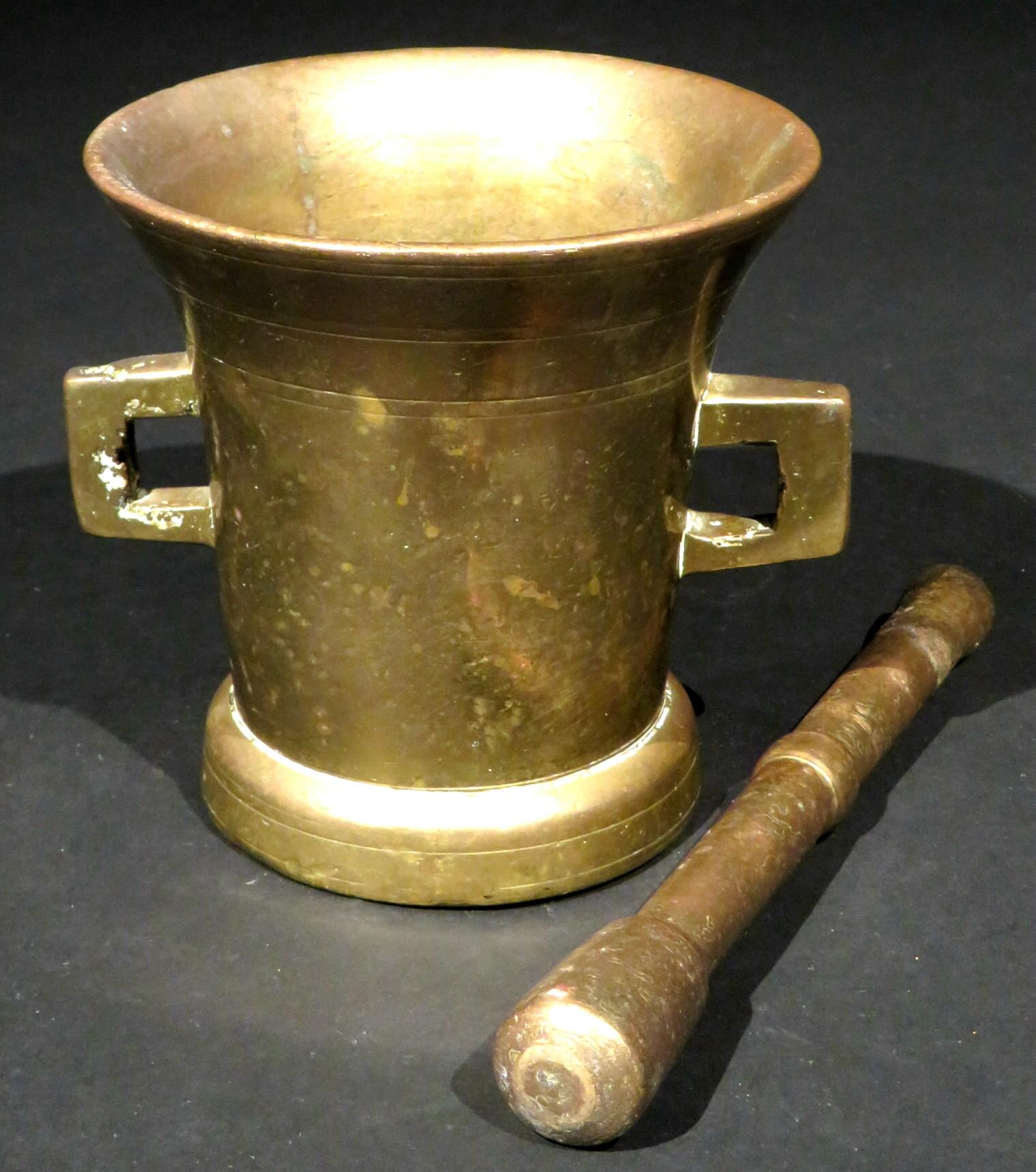 The cast body of flaring form with incised ring-turned detail, rising from a compressed foot and sided by twin open handles, together with what appear to be its original pestle.
Combined weight, 6 lbs.

