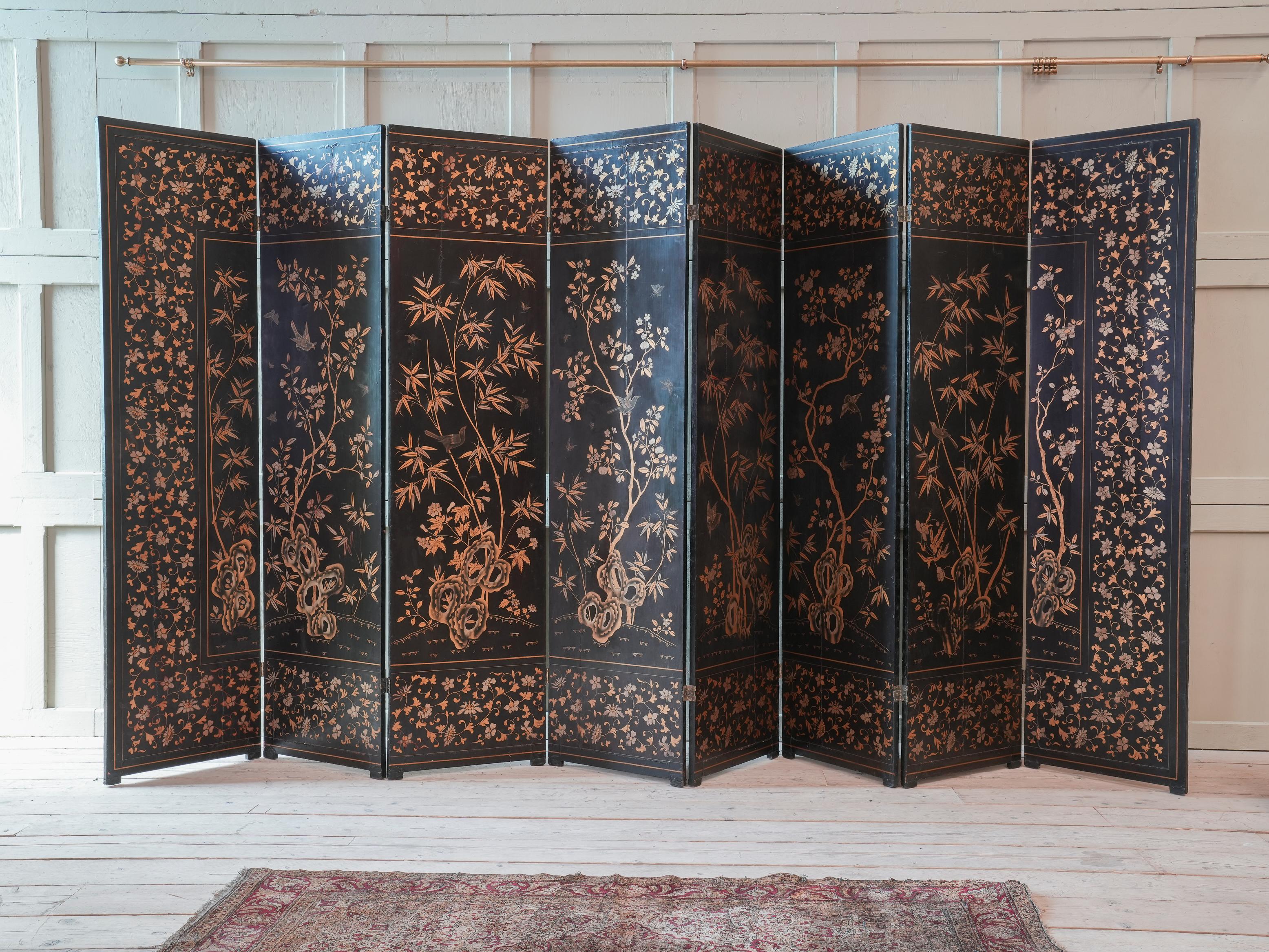 The black lacquered timber panels decorated with a sprawling landscape, figures, temples, animals, pagodas and junks within a border of trailing vines with exotic birds and butterflies in shades of black on a gold ground.

The reverse decorated