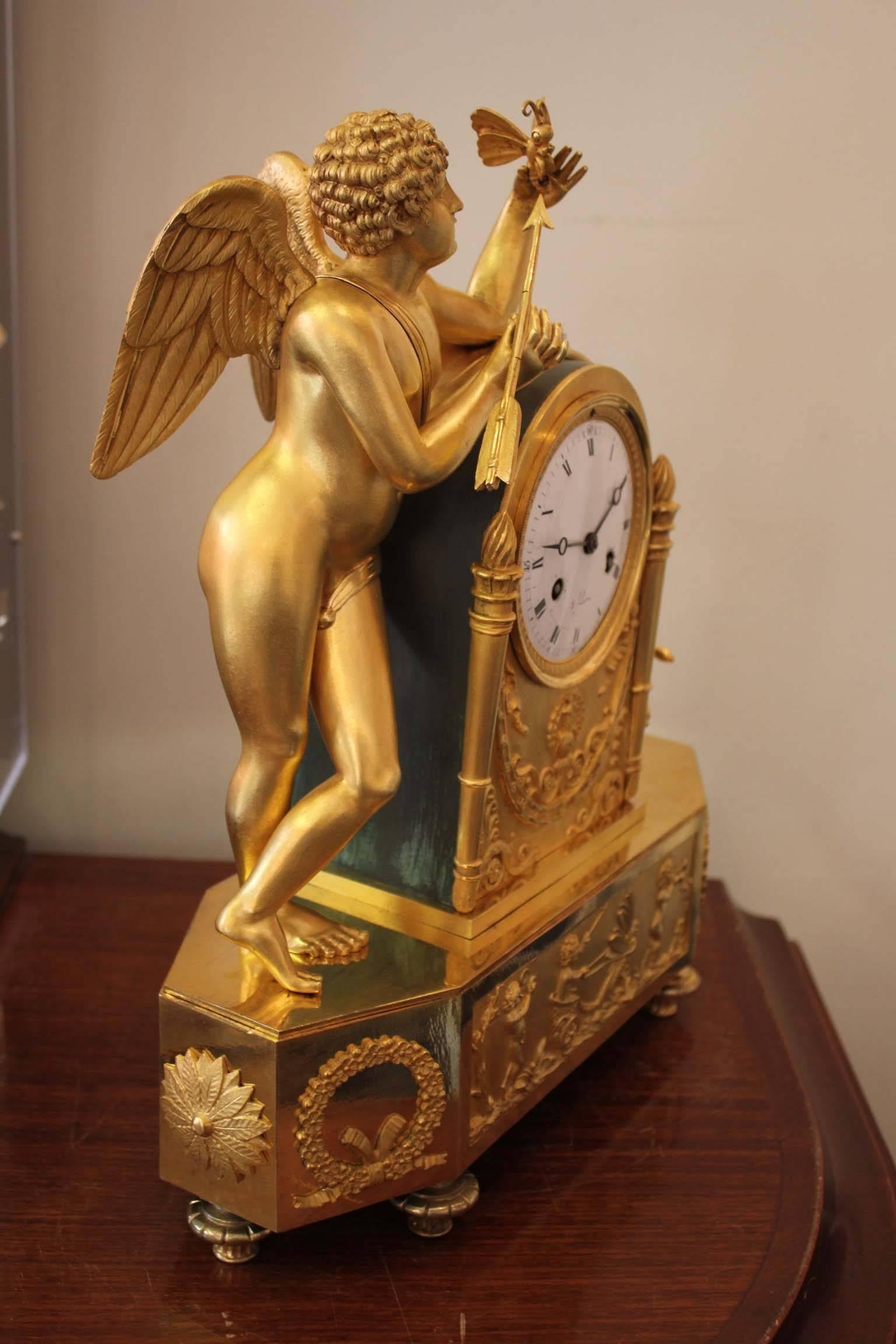 Beautiful clock representing an Allegory of Love. Made in gilt bronze and chiseled brass, partially matified, on a rectangular plinth base with musician puttis surrounded by flowers and ribbons. Cupidon holds a butterfly in his hand, and is about to