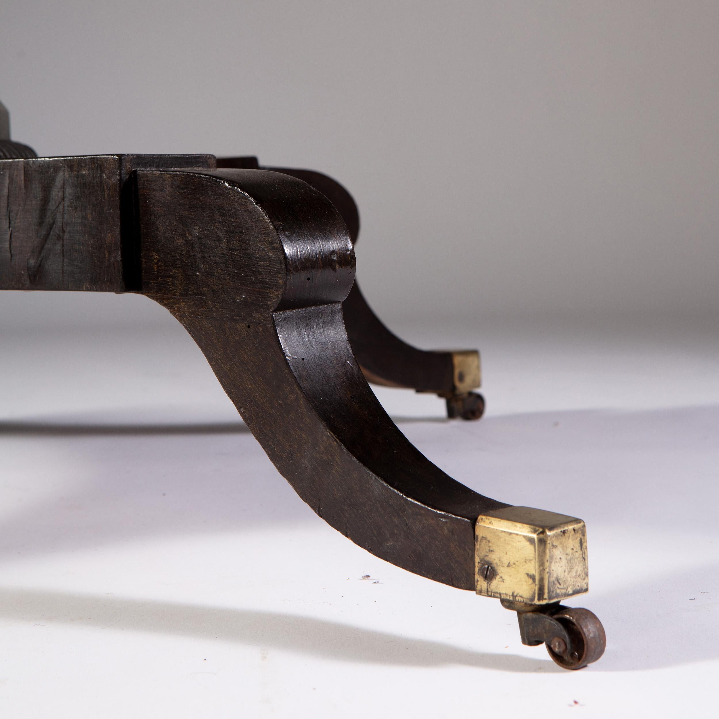 An early 19th century ebonized center table, with burr yew wood edge, and carved pilaster stem, all supported on a quadruped base with sabre legs terminating in brass castors. Attributed to William Trotter of Edinburgh.