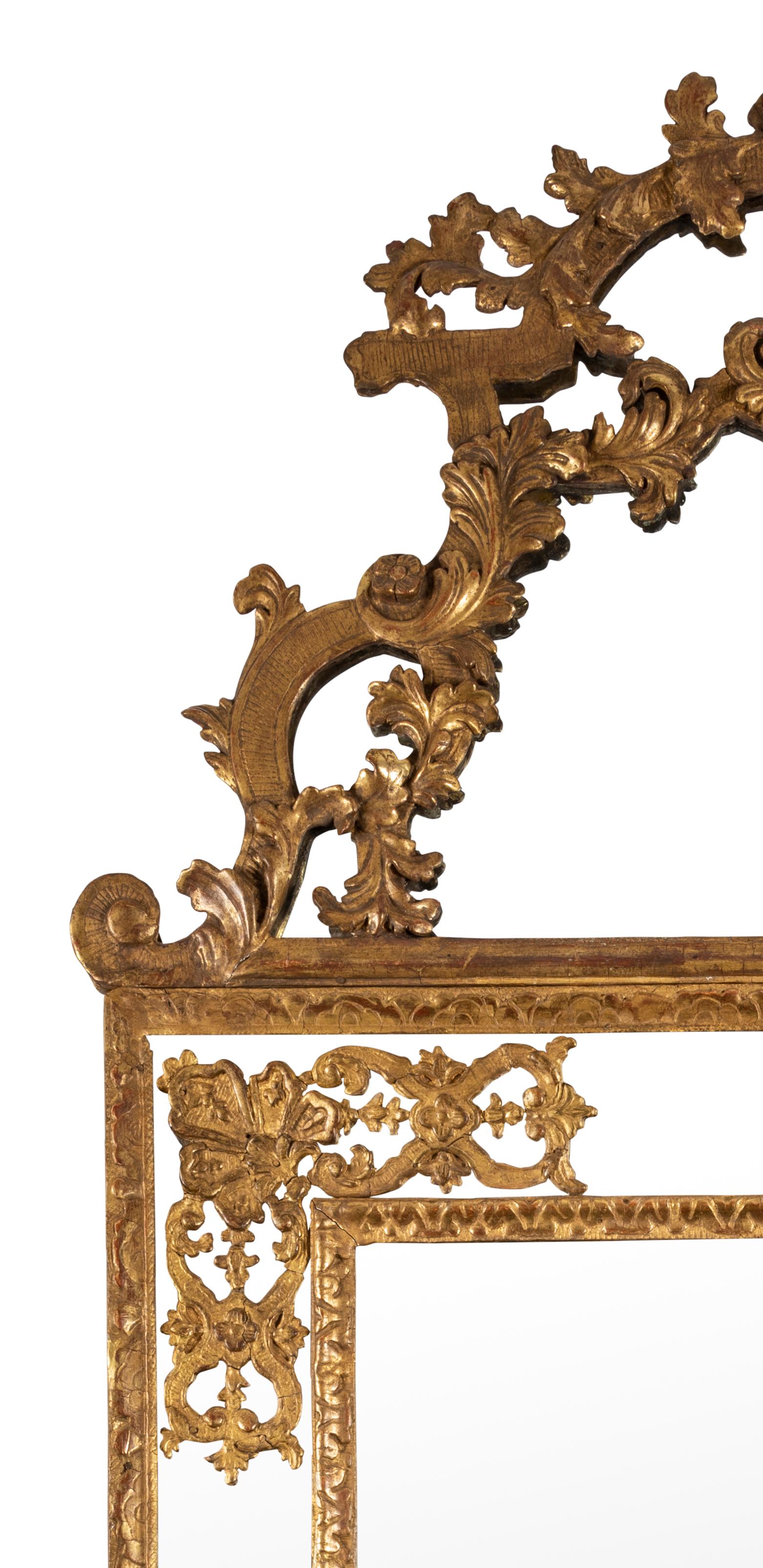 The bevelled rectangular central plate bordered by a water leaf moulding, within a mirrored surround applied with a gilt anthemion over an arrangement of pierced scrolls to each corner, extending to a stylized floral gilt moulding, rising to a