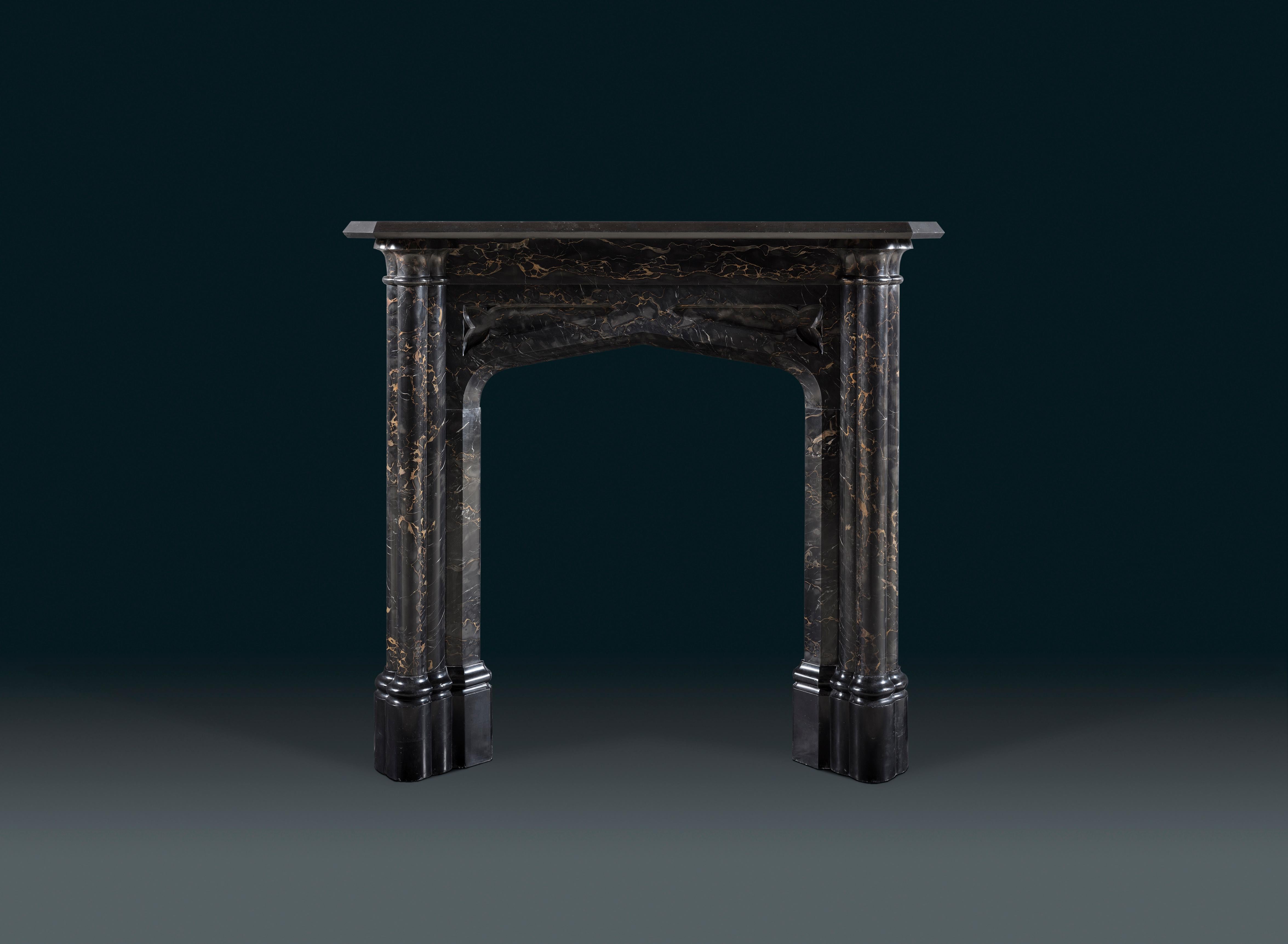 A rare early 19th Century Gothic Revival chimneypiece in Portoro and Belgium Black marbles. The quatrefoil column jambs flank a sloped Gothic arch opening, on tall moulded footblocks.