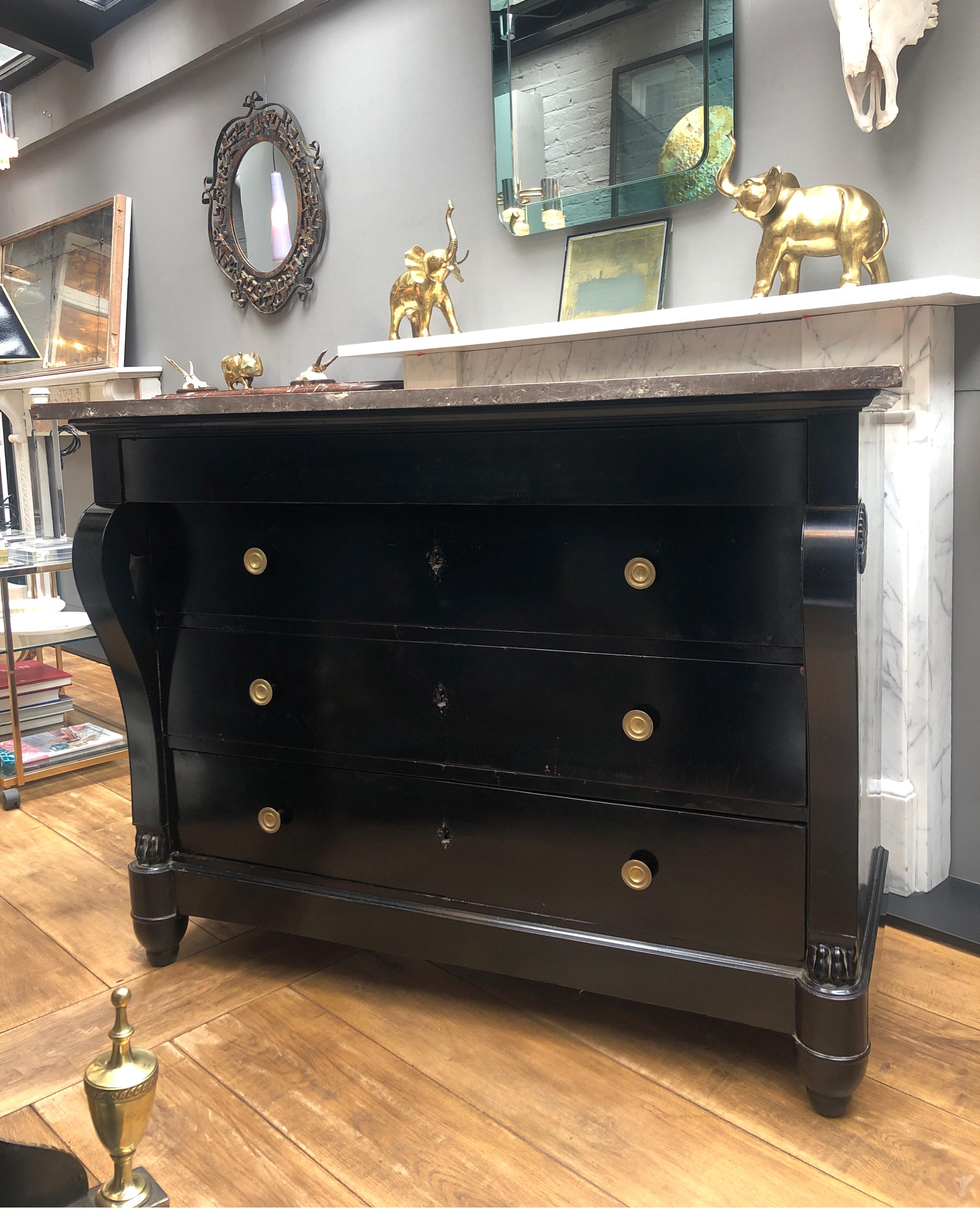 An Italian early 19th century ebonized marble-topped commode with a bank of 4 drawers the top drawer without handles. The brass circular engraved handles on the remaining three drawers. Having console front supports with circular patarae to sides