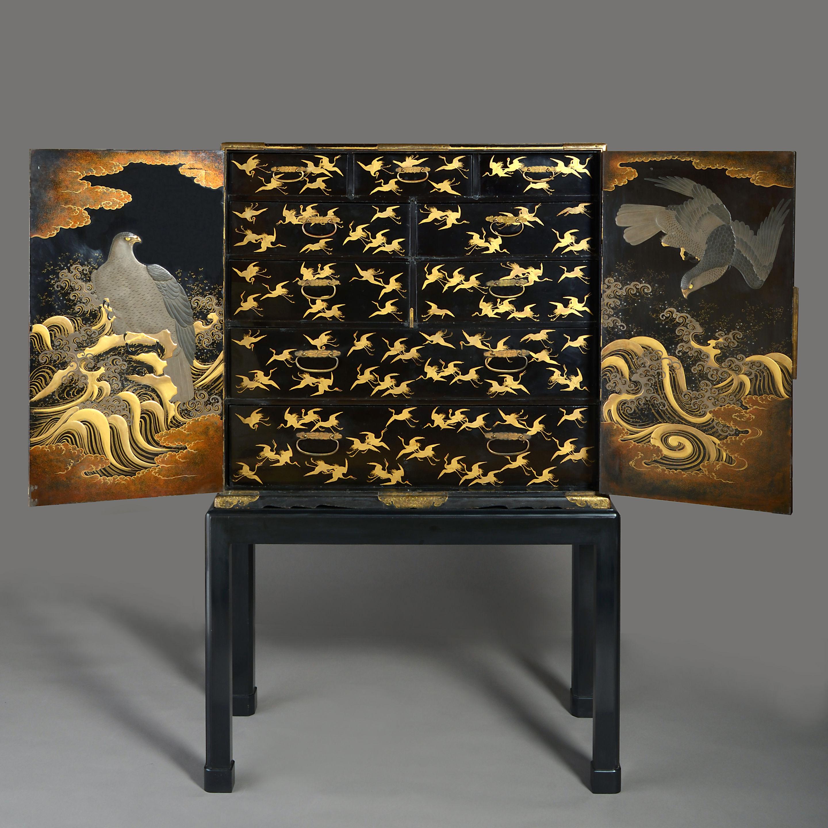 An early 19th century lacquer cabinet of great scale the front having two doors, each with a rectangular panel with re-entrant corners and decorated with a view of mount Fuji, a flock of cranes, before lowlands and a coast line with trading ships in
