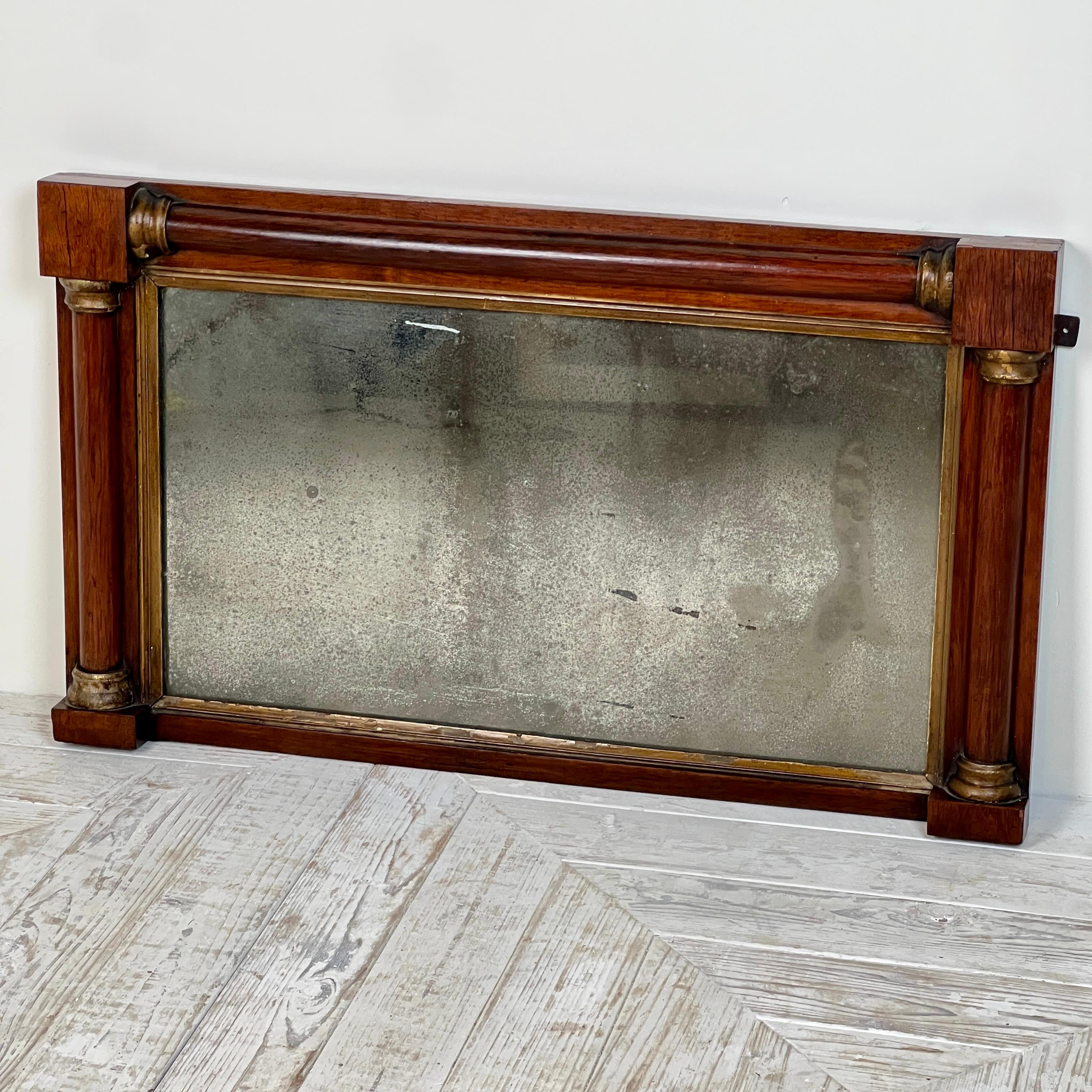 Specchio a ribalta in mogano dei primi del XIX secolo. La cornice in mogano è formata da colonne in stile architettonico con terminali decorativi dorati. L'incantevole specchio consumato dal tempo è incorniciato da una semplice sottoveste dorata per