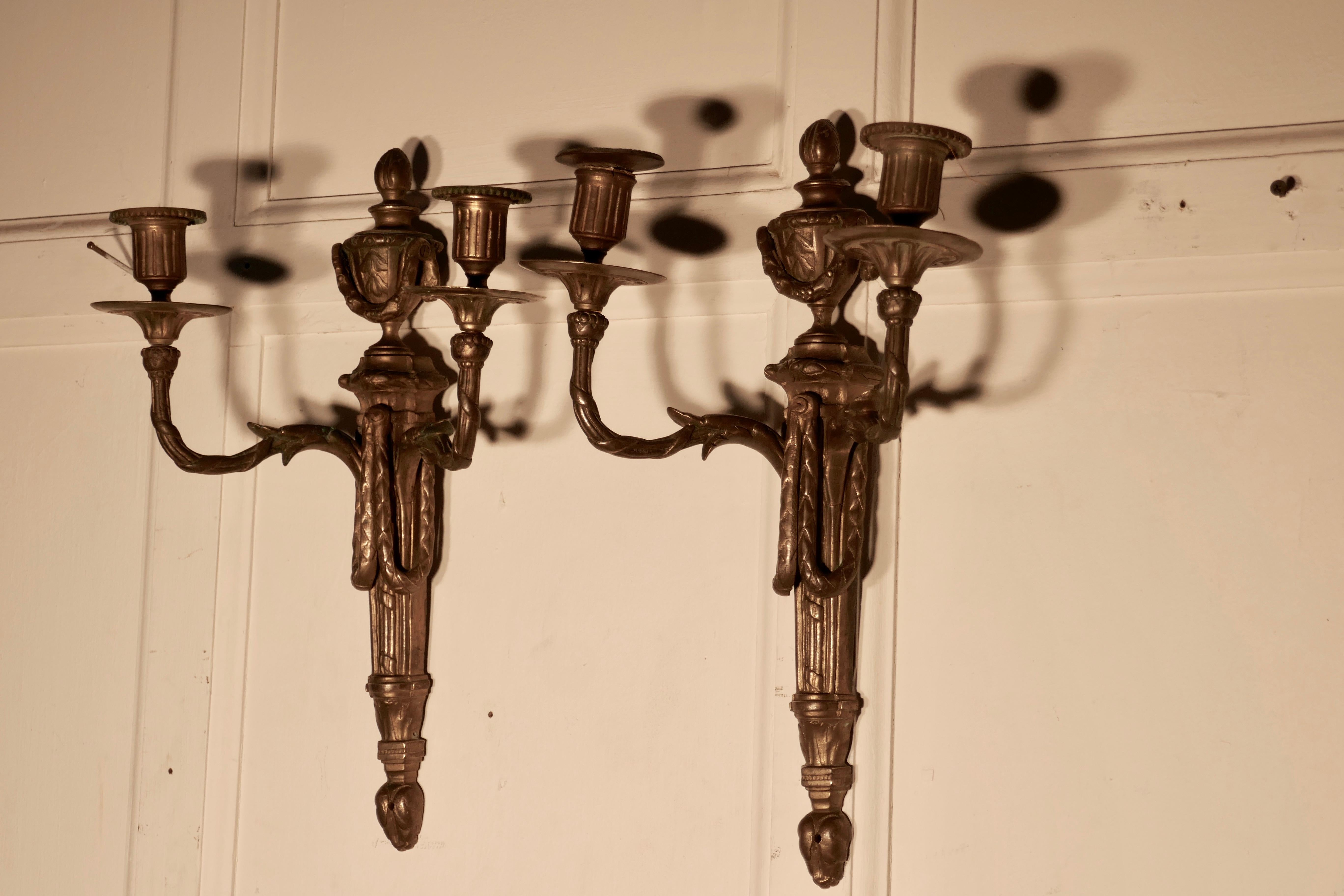 An early 19th century pair of french brass twin wall sconces

A pair of large French gilded twin arm antique wall candle sconces, the ornate leaf scrolling arms are decorated with swags and urns, they are still with their original candle sconces
