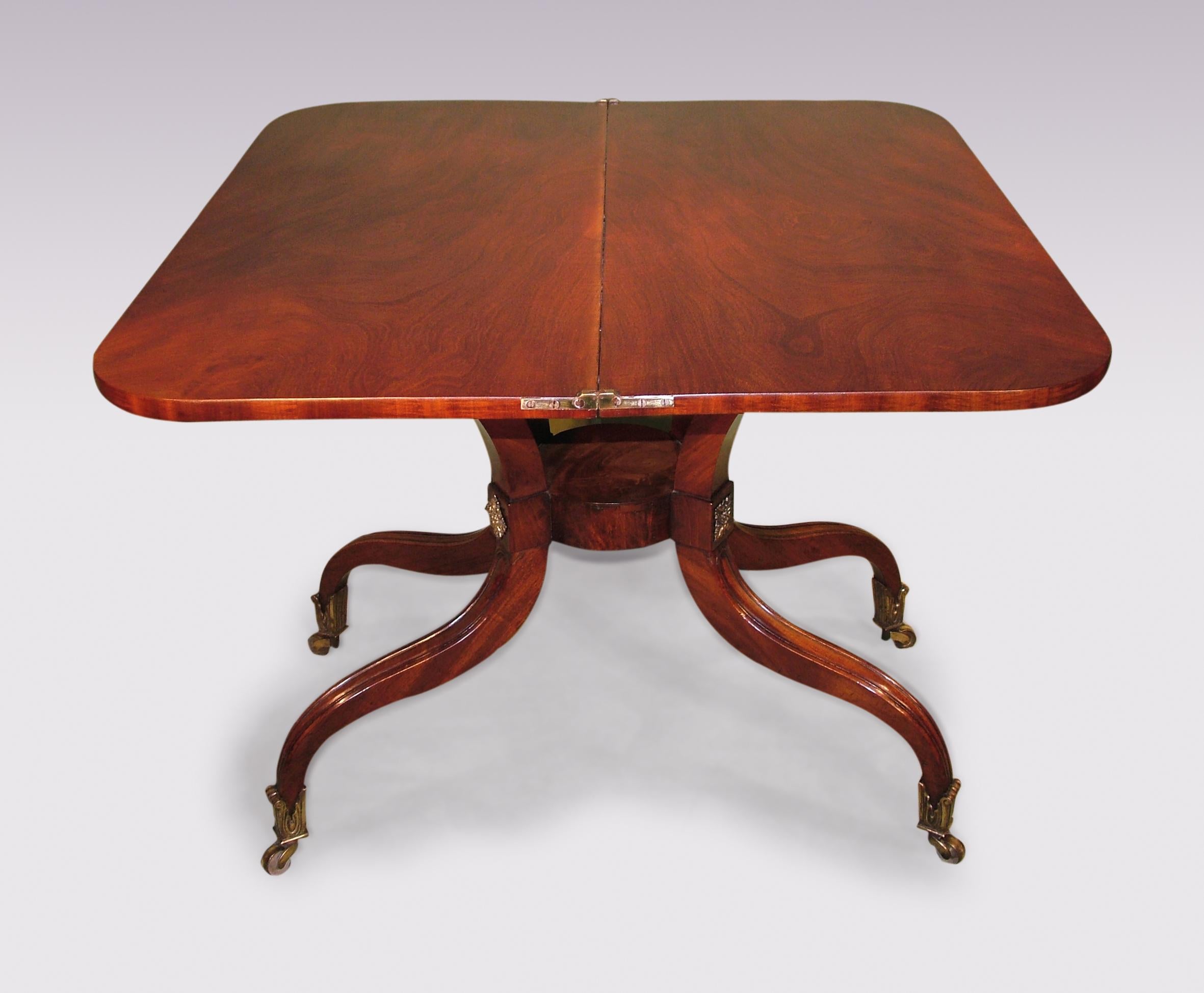 An early 19th century Regency period well-figured mahogany tea table, having rectangular top above narrow, shaped frieze raised on brass-mounted and moulded scroll umbrella-shaped legs joined by circular platform ending on original foliate castors.