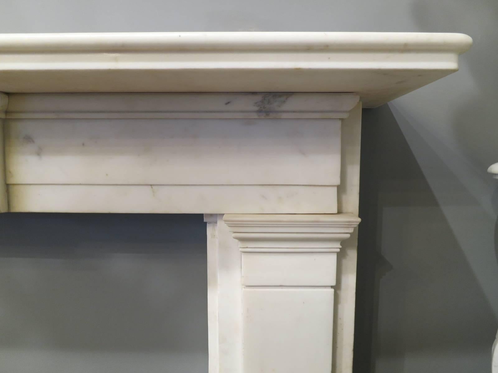 An architecturally designed Regency period fireplace in statuary white marble. The pilaster jambs with moulded and stepped capitals, supporting a stepped long frieze with plain centre tablet to centre. The mantel wide and generous with a bull nose