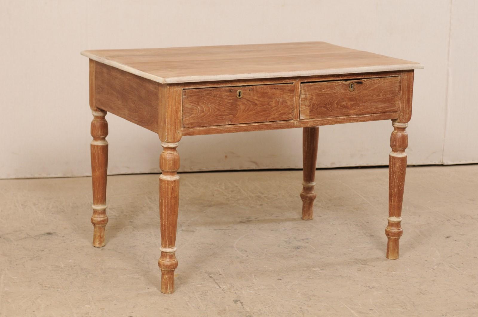 A British Colonial occasional table from the early 20th century. This antique table from India features a slightly overhanging, rectangular-shaped top, resting above a plain skirt which houses two drawers at one long side, and is raised upon four