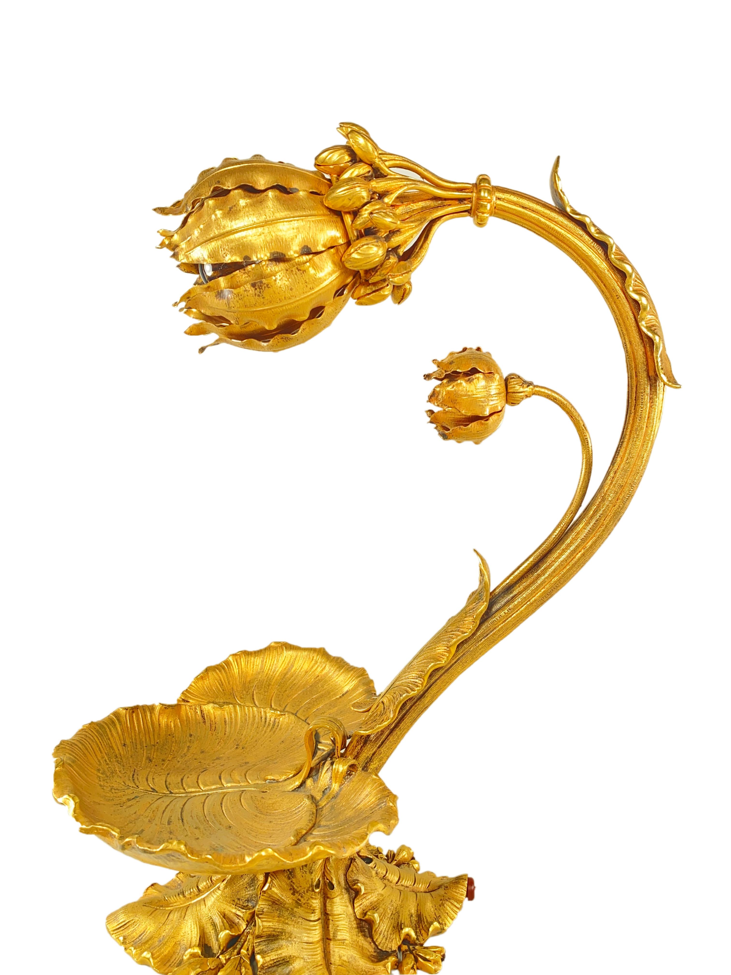 A French Art Nouveau early 20th century gilt bronze desk lamp decorated as a budding flower accentuated with lily pad decoration as a tray leading with leafage and floral buds from the arch leading into a budding flora shaped gilt bronze shade. The