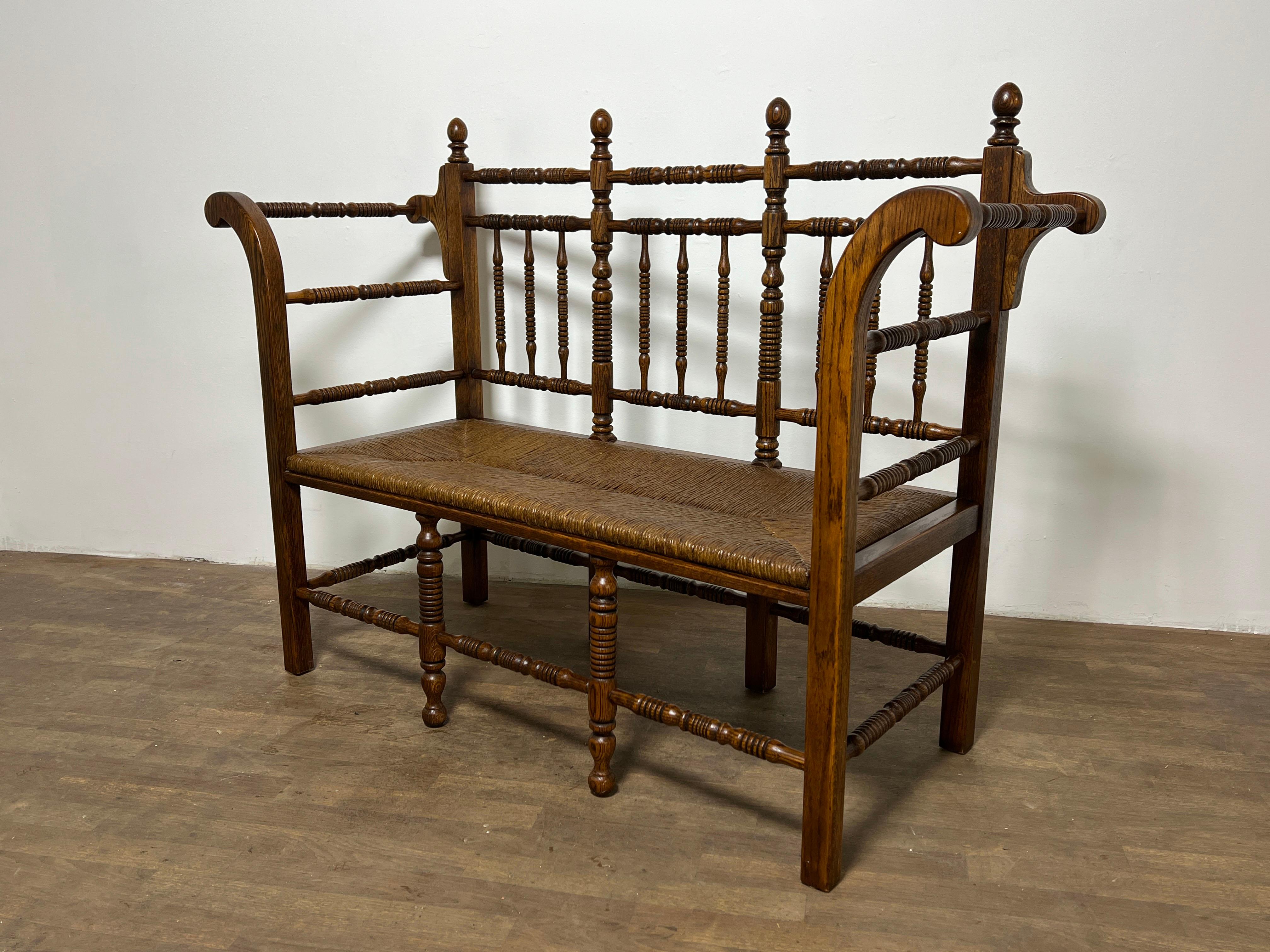 Antiguo banco catalán de principios del siglo XX, de roble finamente torneado, con asiento de junco tejido.