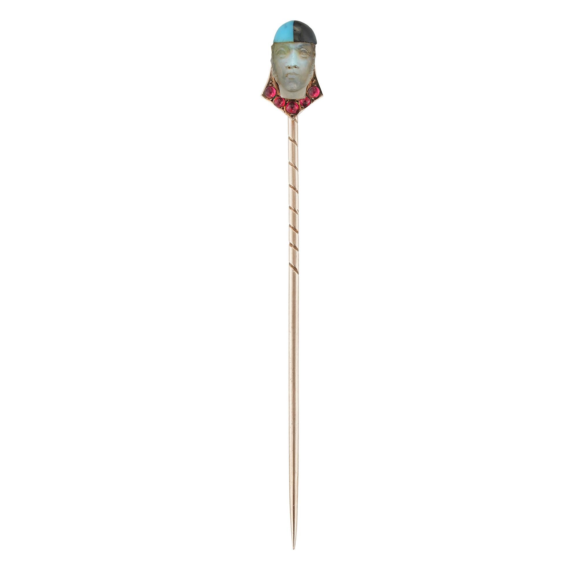 Épingle à bâton en pierre de lune et rubis arlequin du début du 20e siècle, la pierre de lune sculptée de façon réaliste sous la forme d'une tête d'arlequin avec un chapeau émaillé bleu et noir, le collier flanqué de cinq rubis ronds taillés en
