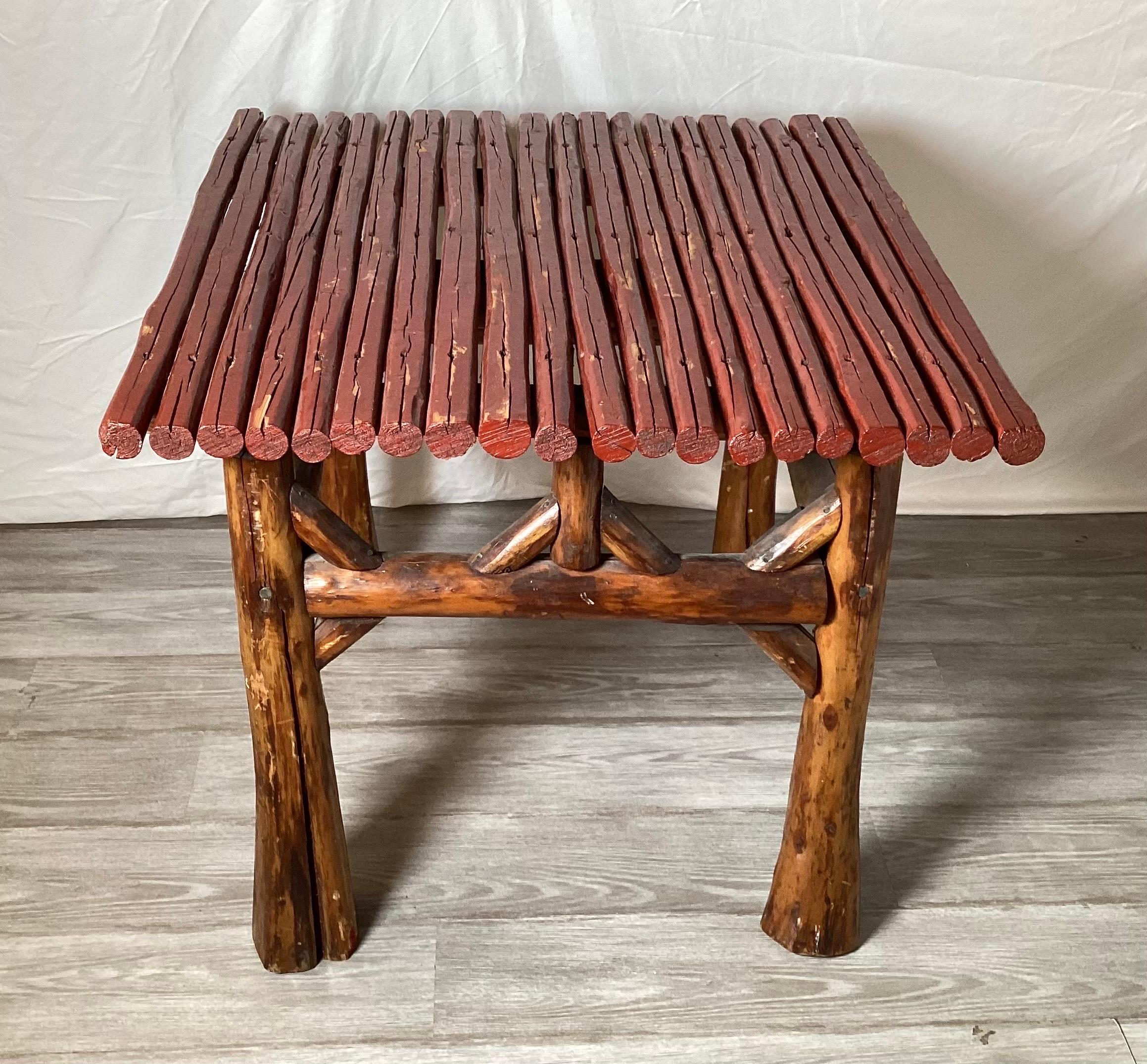 A square Adirondack table with red painted top. This sturdy table with wood finished legs and red pained branch top. The top with wear and old splits, but sturdy and usable. 27 inches tall, 30 inches square.