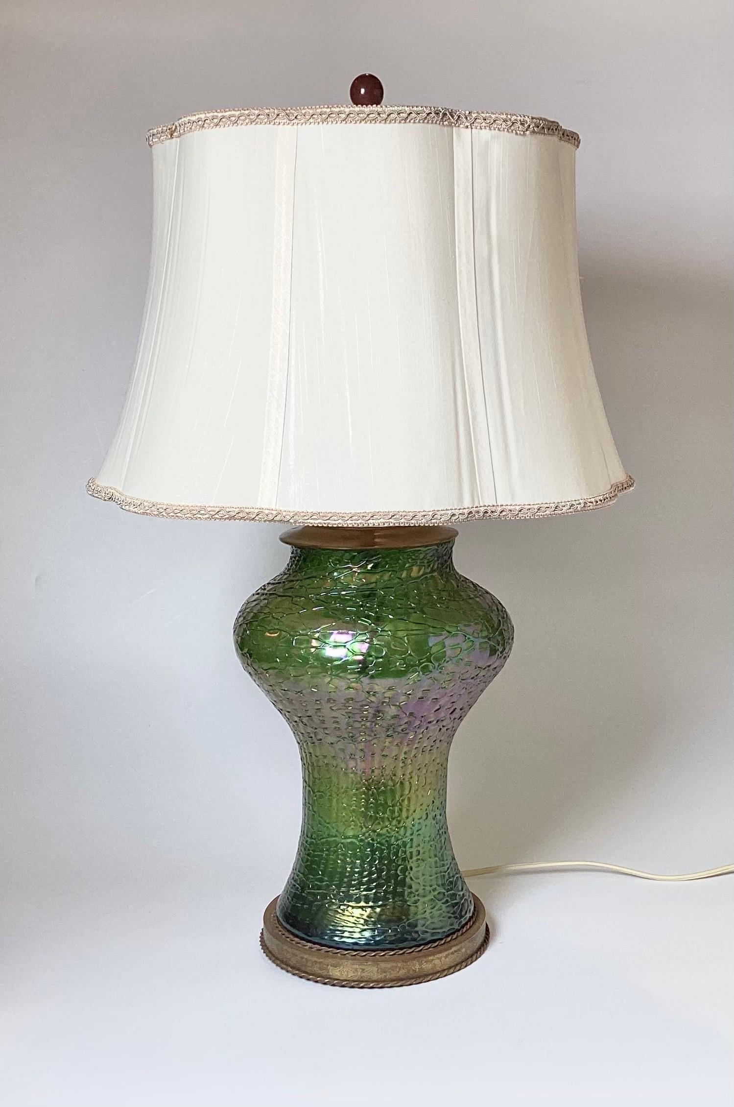 Elegant hand blown iridescent green glass lamp with la ficelle surface. The shapely body with green background with an overlay web effect on the surface. The top and bottom with naturally aged brass patinated mounts. The lamp with two sockets, one