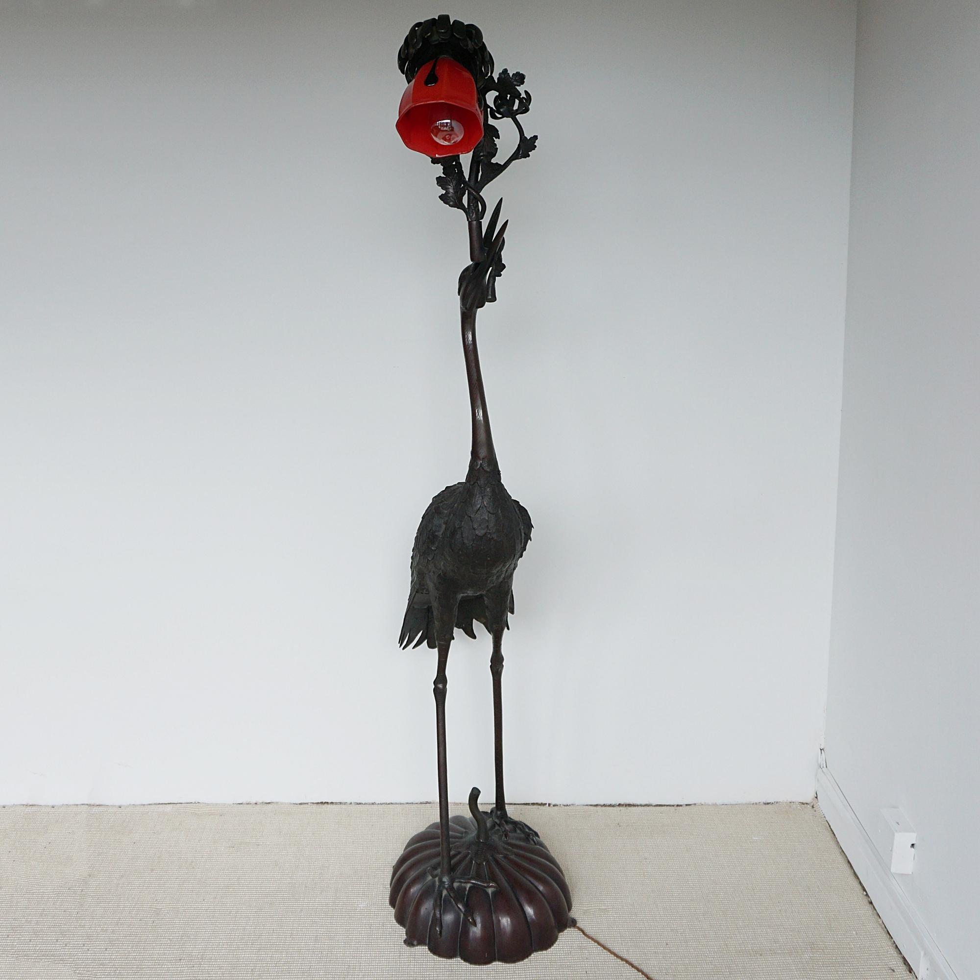 Lampadaire en bronze du début du 20e siècle de la période Meiji. Grue couronnée rouge, finement détaillée, debout sur un pad de nénuphar, une branche dans le bec, tenant un abat-jour en verre d'origine en forme de fleur de lotus rouge.

Dimensions :