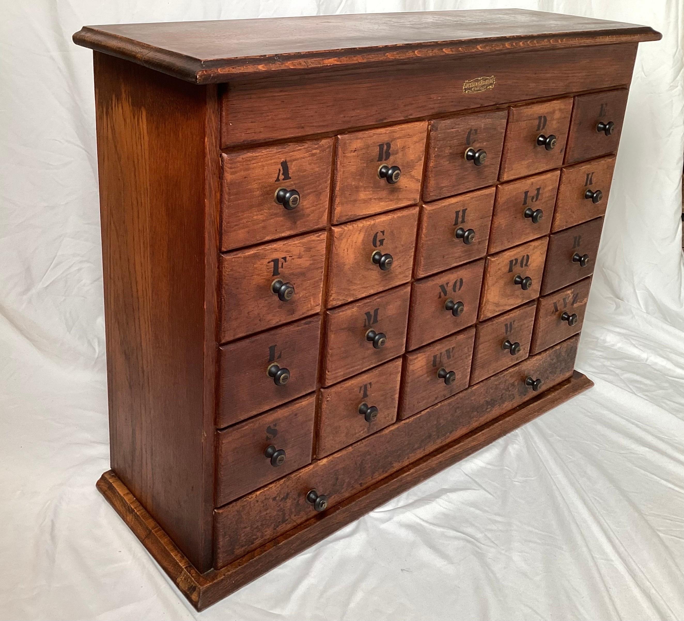A Circa 1900 American Oak apothecary cabinet.  The chest with 20 square drawers and one long bottom drawer, the top with a lift up lid for extra storage.  Each drawer with a stenciled A-Z label.. 