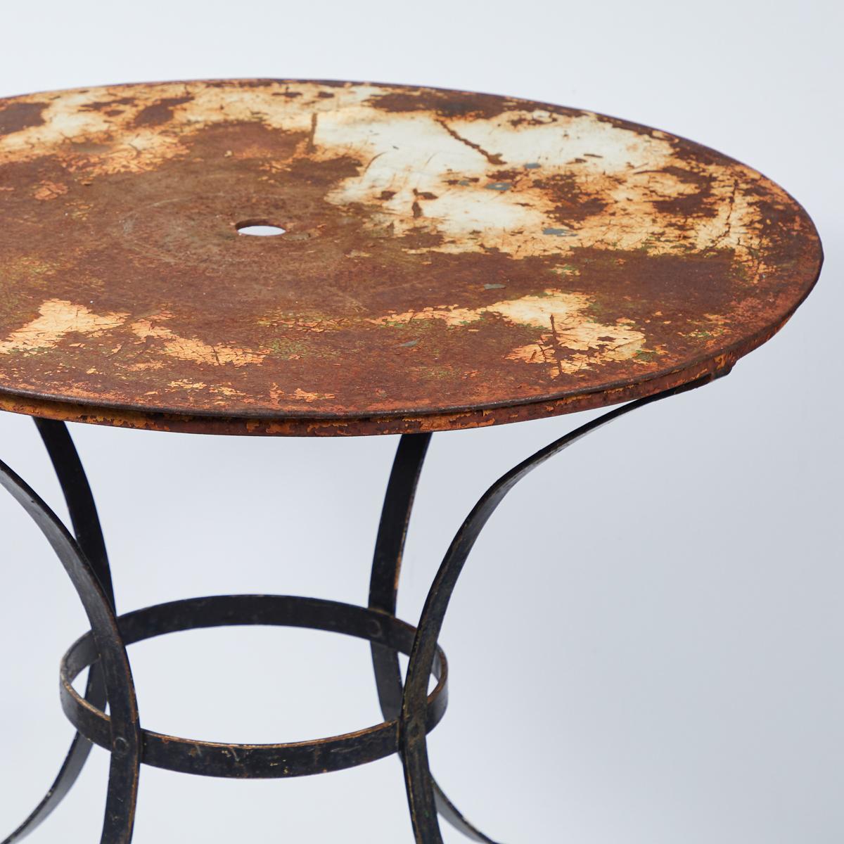 Early 20th-century English garden table with a round top showing traces of white paint. Set on a wrought-iron silhouette base, the piece a rustic, natural patina, and would make charming addition to any garden, patio, terrace, or outdoor space.
