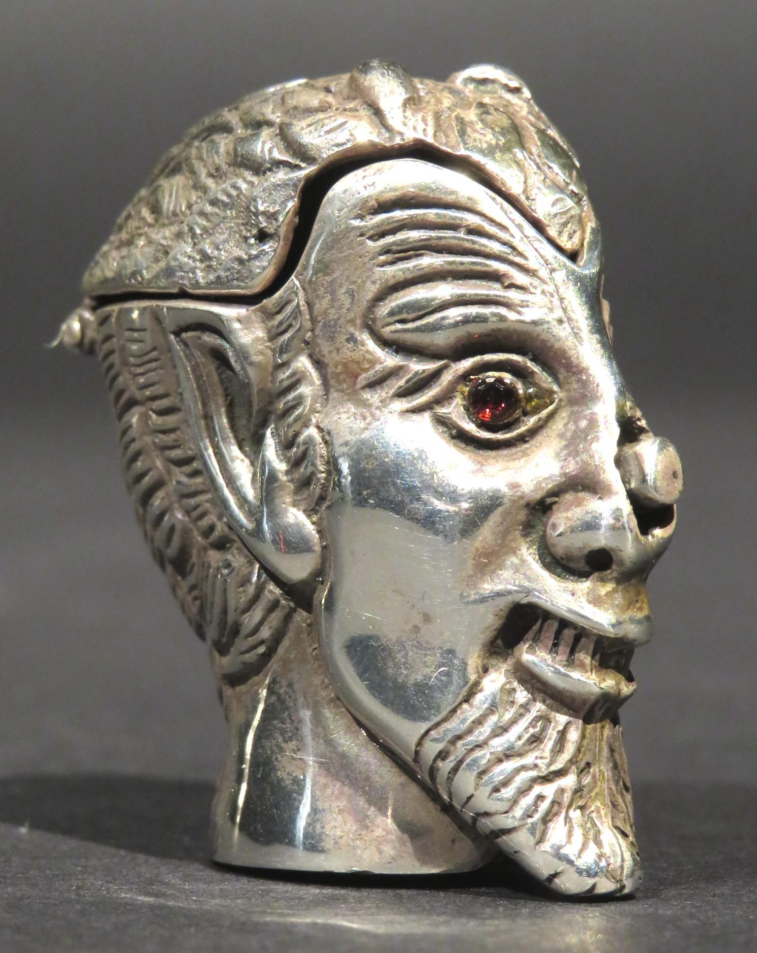 An amusing sterling silver novelty vesta case / match safe in the form of a devil's head. The face having an expressive sardonic grin and eyes inset with red stones. The crown of the head opening on a sprung metal mechanism activated by depressing a