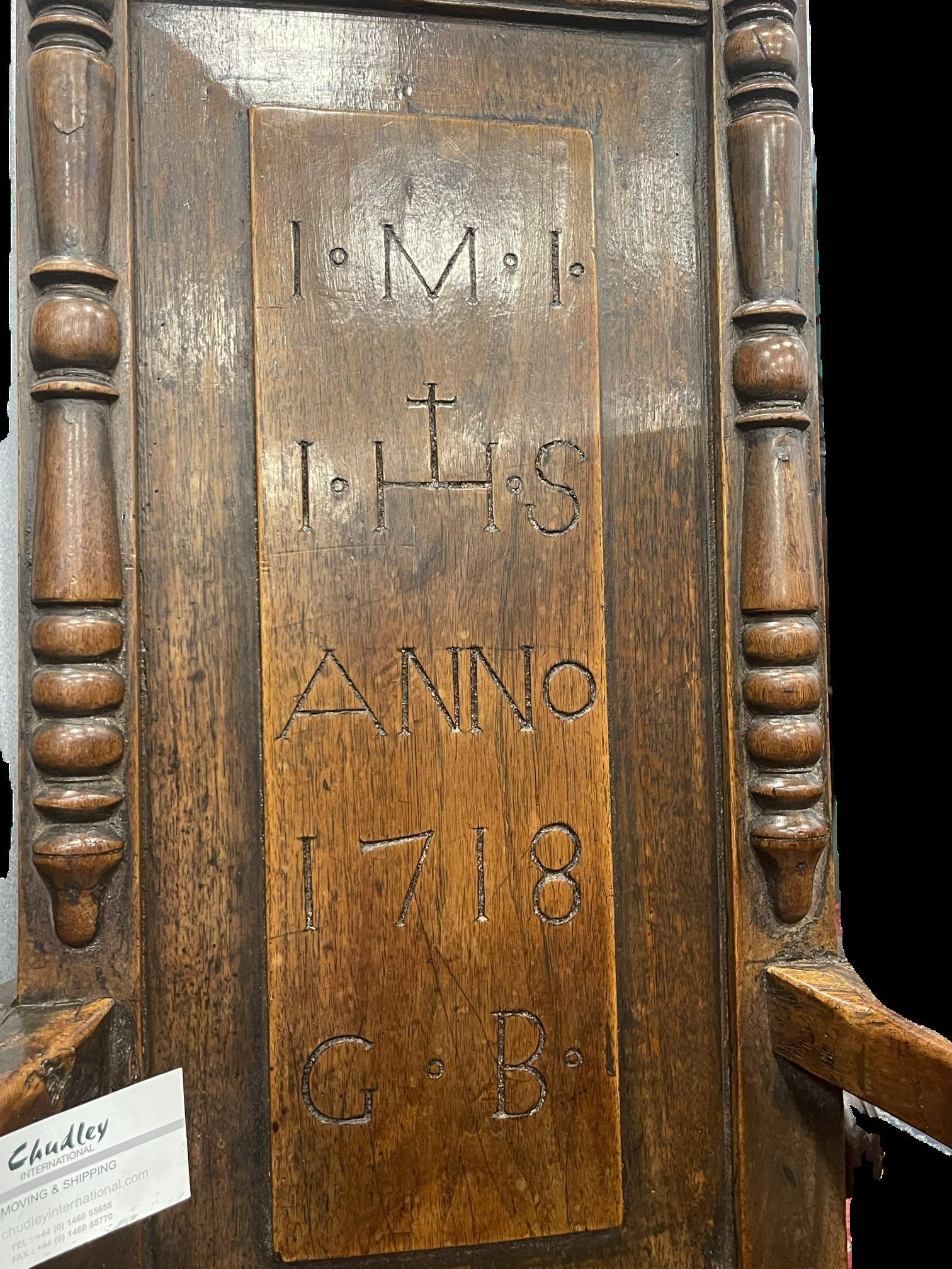An exceptional example of an early and rare caquetoire chair with carved cresting over an unusually narrow back, inscribed ‘I.M.I., I.H.S., ANNO 1718, G.B.’, with large outward scrolling arms, on block turned supports, joined by peripheral
