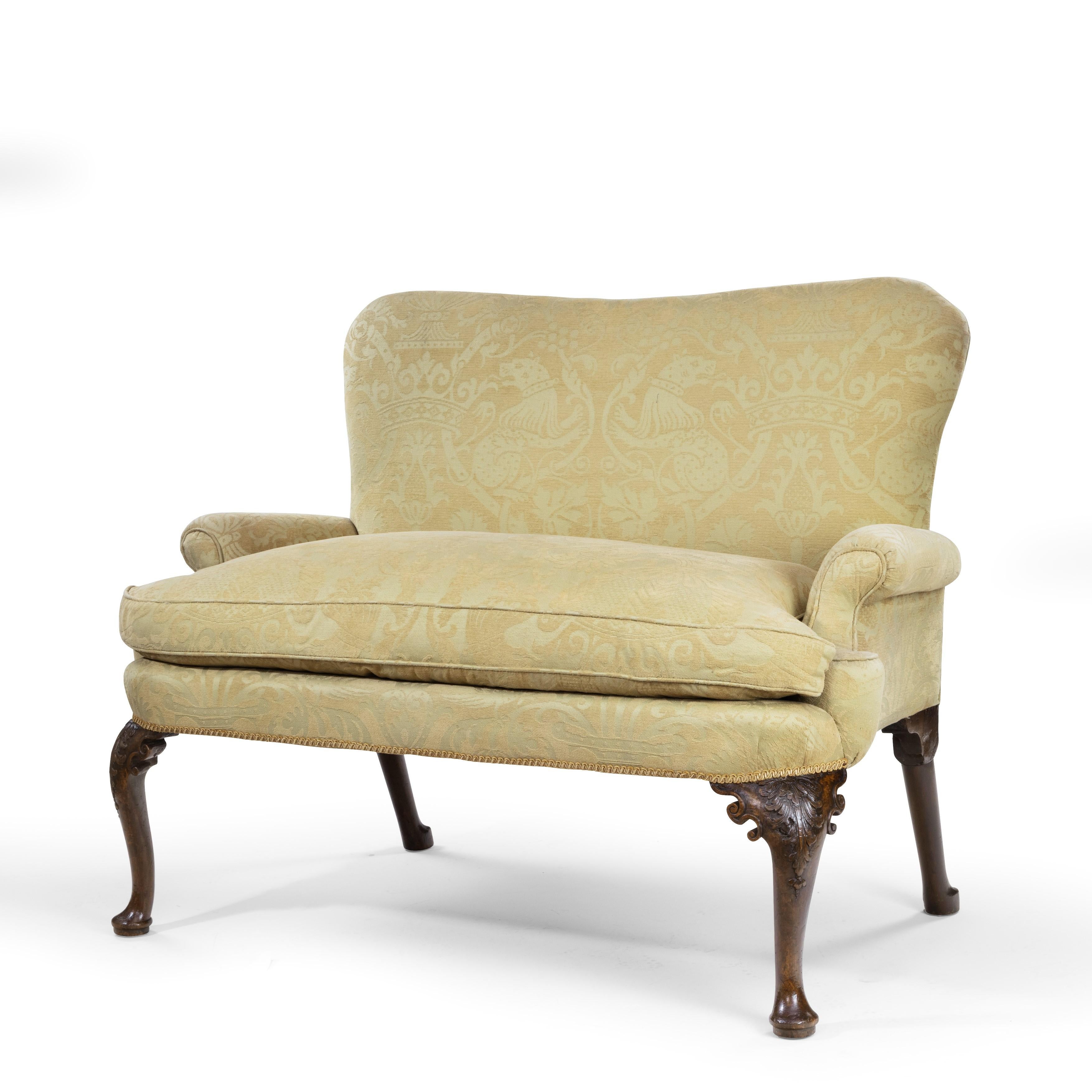 An early George II walnut settee, with a shaped back, scroll arms and a single seat cushion, the cabriole legs carved with shells on the knees and terminating in pad feet and outswept back legs. English, circa 1730.
   