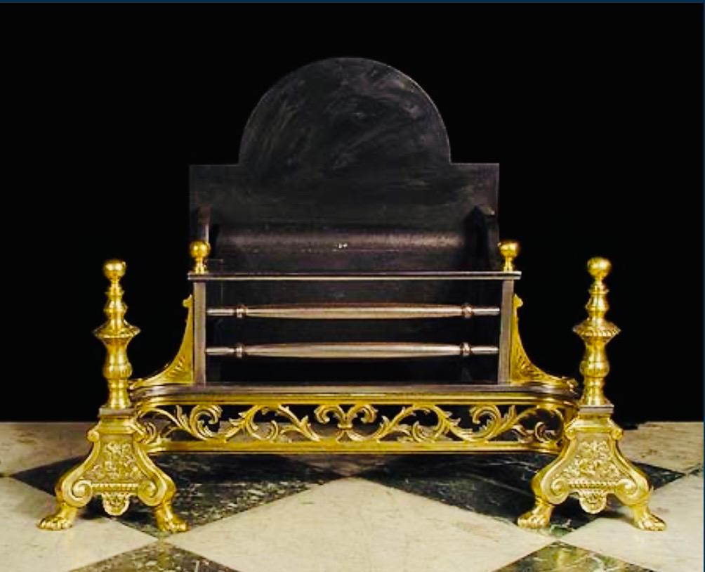 An early Georgian manner brass and steel fire grate basket, a high arched back with a polished three barred grate, below an apron of polished scroll cut brass flanked by tall baluster andirons with floral embellishments resting on lion paw
