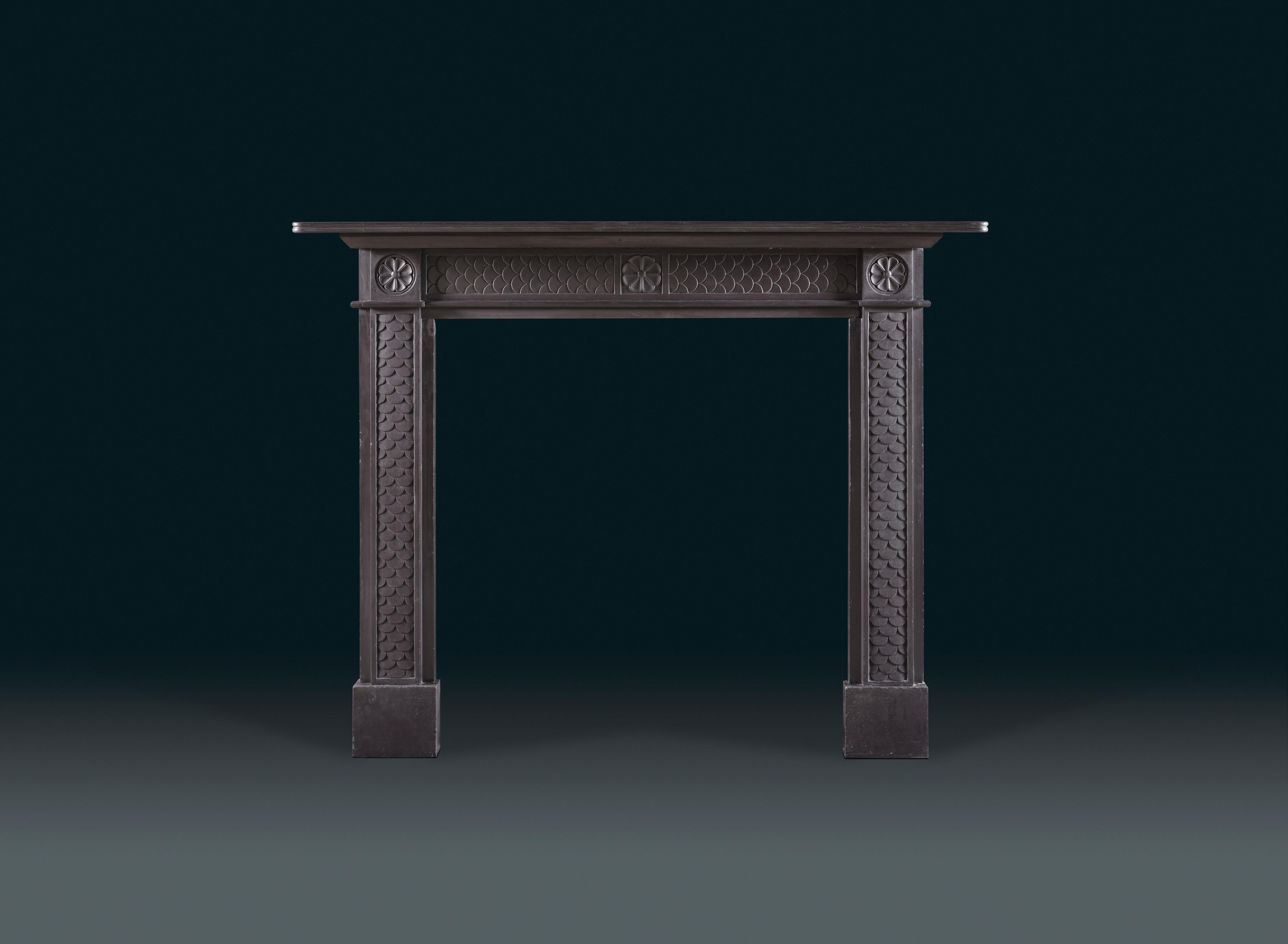 A refined early Regency Welsh chimneypiece carved in slate.
A fish-scale detail runs through the surround, and a patera motif is shown in the corner blocks and at centre of the header. The thin shelf together with the proportions of this design are
