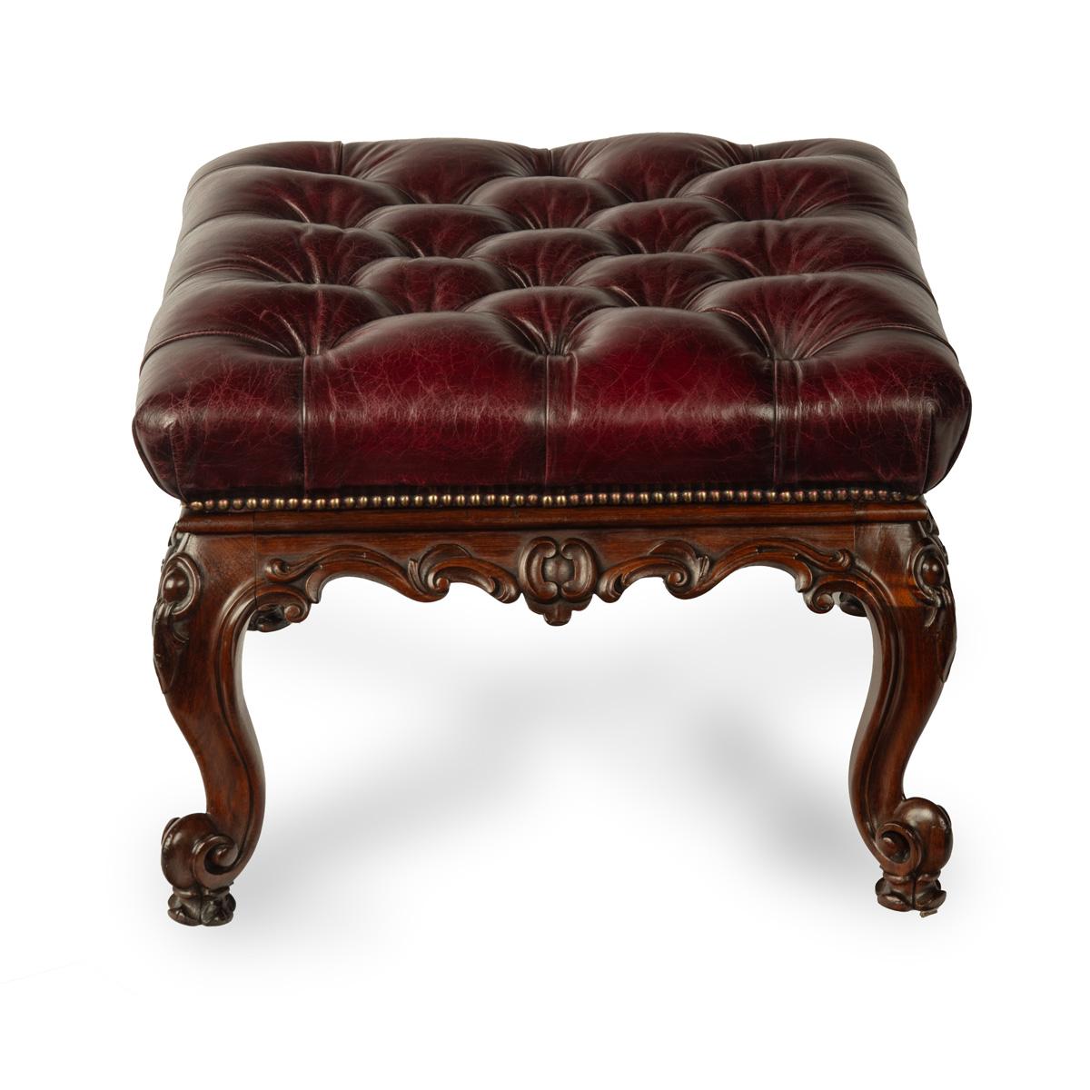 An early Victorian leather-upholstered rosewood stool, of square form, the drop-on top re-upholstered in deep buttoned burgundy leather, raised on bold cabriole legs, the seat rail and feet carved with scrolls and oval bosses.  English, circa 1850.

