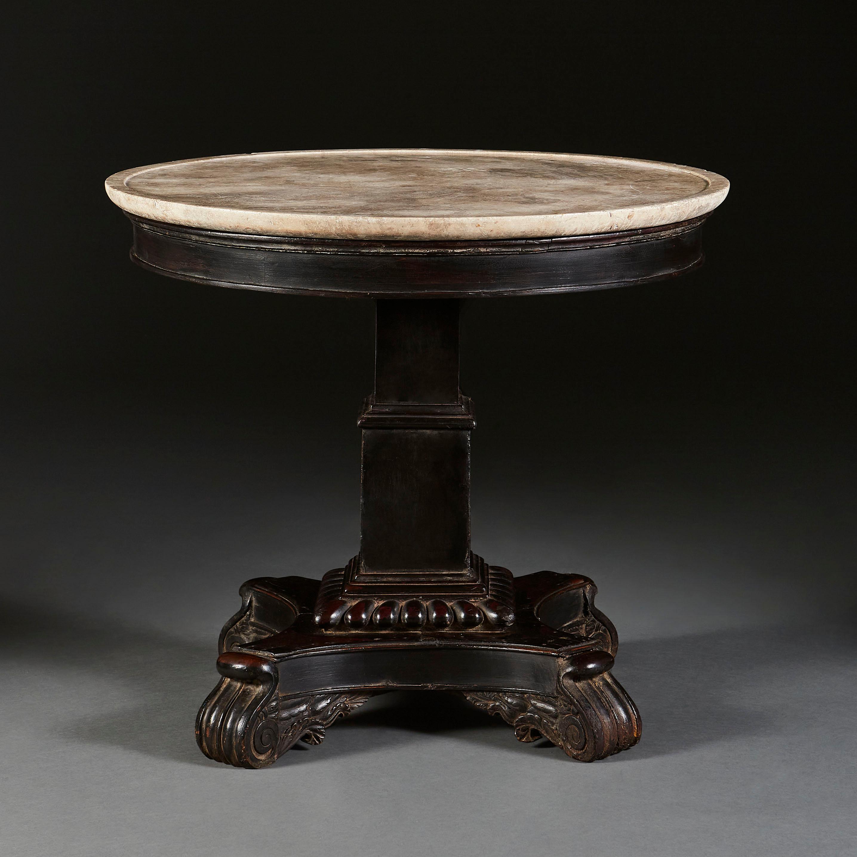A mid-19th century Anglo-Indian centre table with carved ebonized pedestal base, supported with four scroll feet, with off-white figured marble dish top.