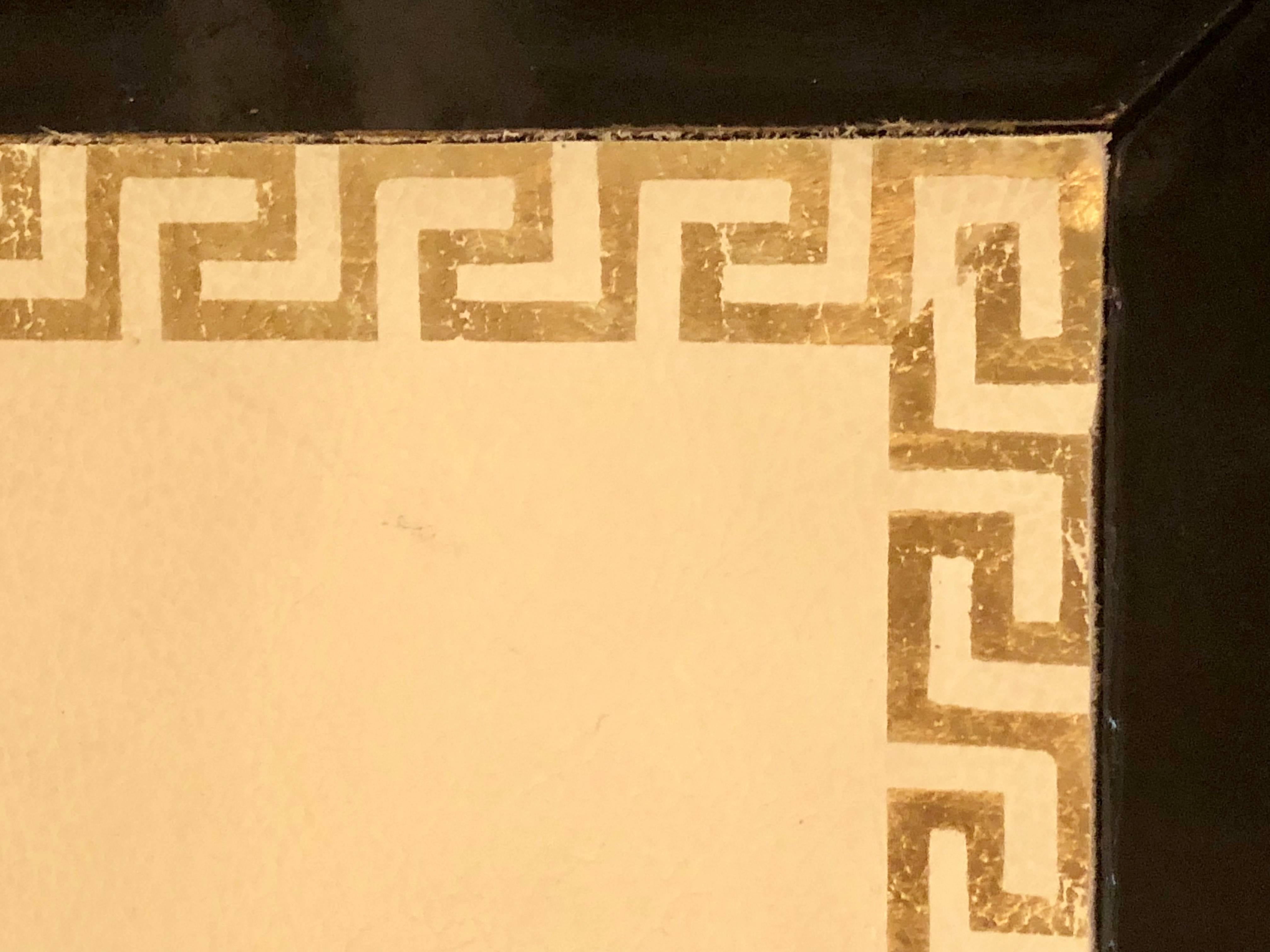 Table basse ébonisée à plateau en cuir de style Jansen avec motif de clé grecque. Cette table intéressante présente des bordures dorées et deux compartiments latéraux coulissants qui s'ouvrent sur un meuble de rangement.