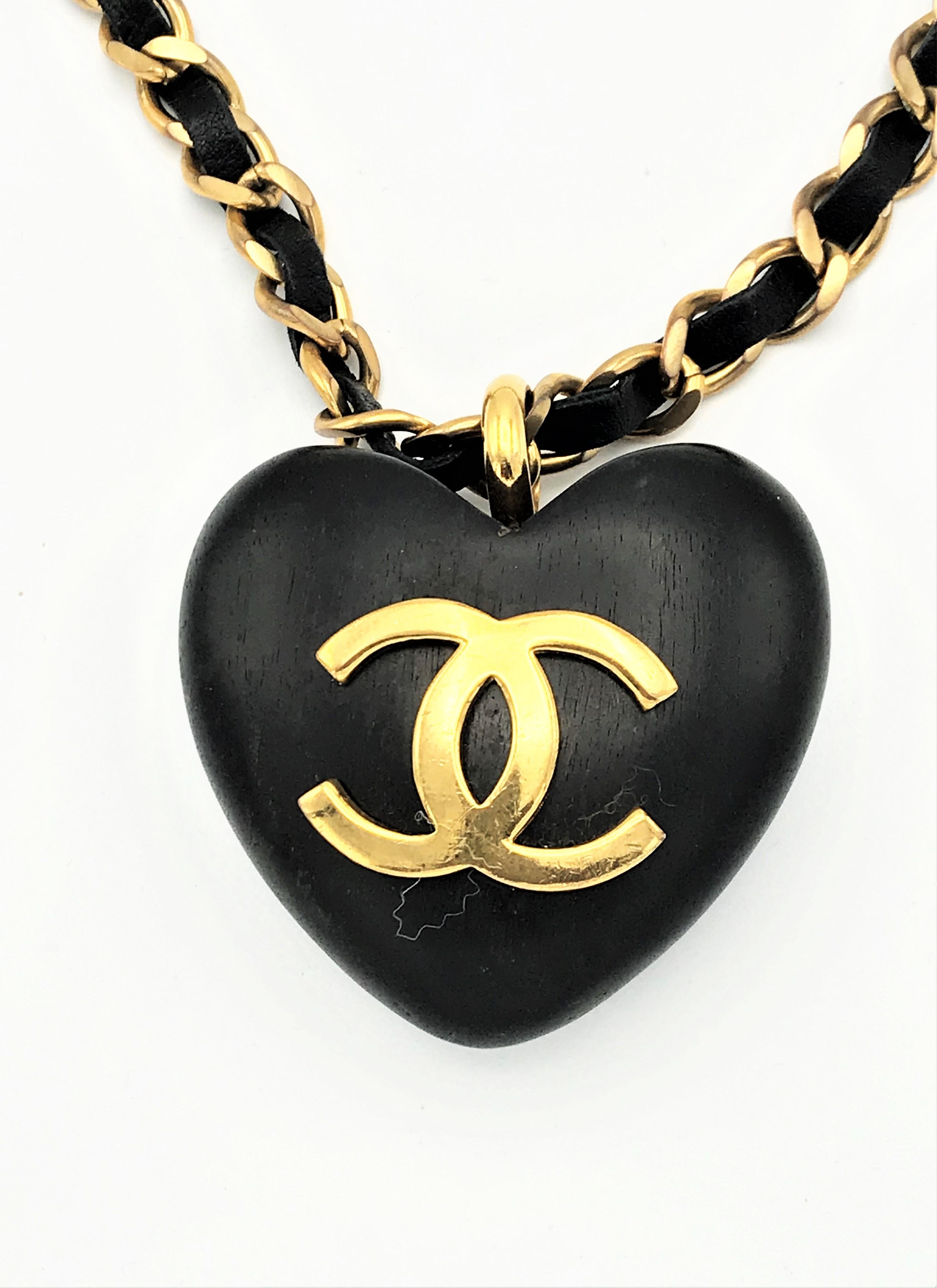 A very ICONIC Ebony Heart hanging on the iconic chain covered with leather. It is designed by Victoire de Castellane 2CC8 = 1990  
The plastic 1,5 cm thick heart pendant is decorated with the gold CHANEL logo and hangs on a 76 cm long chain. It is
