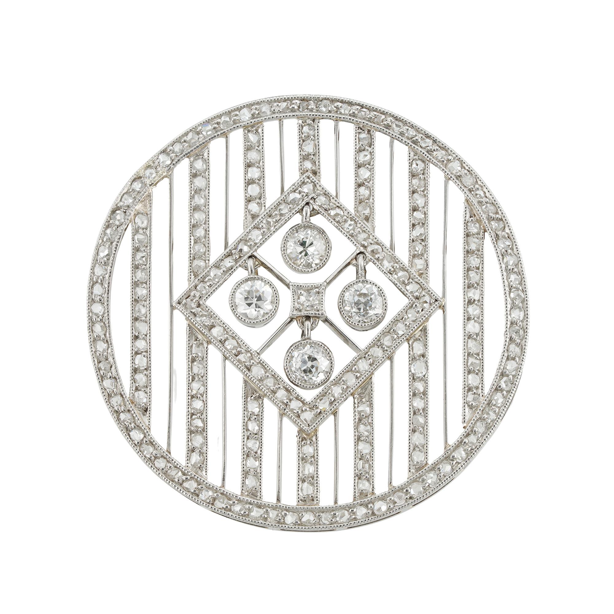 An Edwardian circular diamond brooch-pendant, the round openwork circular frame, with seven vertical diamond-set lines and six knife edge bars in-between, centrally-set with a diamond-set square frame with four old European-cut diamonds estimated to