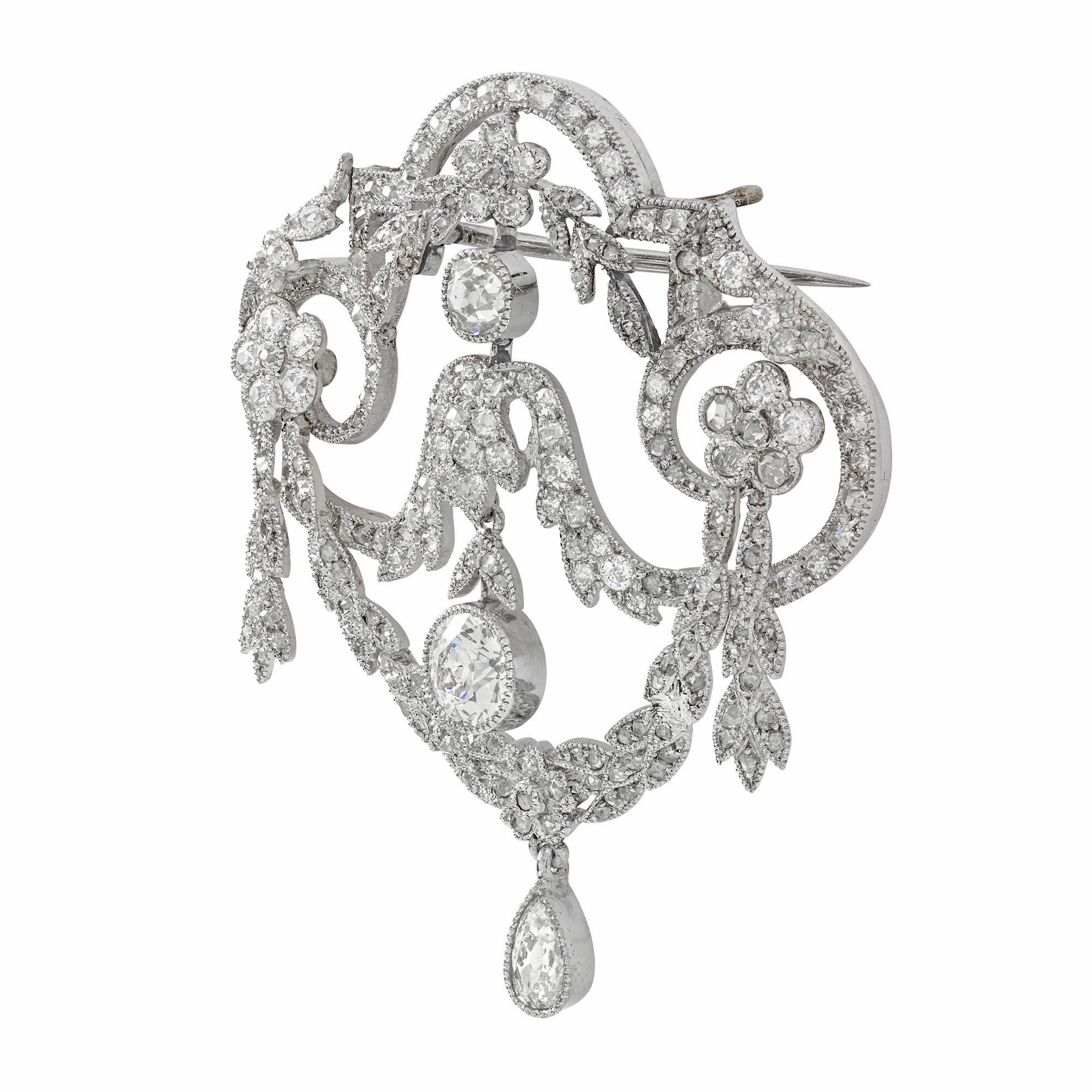 An Edwardian diamond festoon brooch, an old brilliant-cut diamond, estimated to weigh 0.85 carats, surmounted by old and rose-cut festoons with floral clusters and leaf motifs with a pear shape old cut diamond suspended from the central swag,
