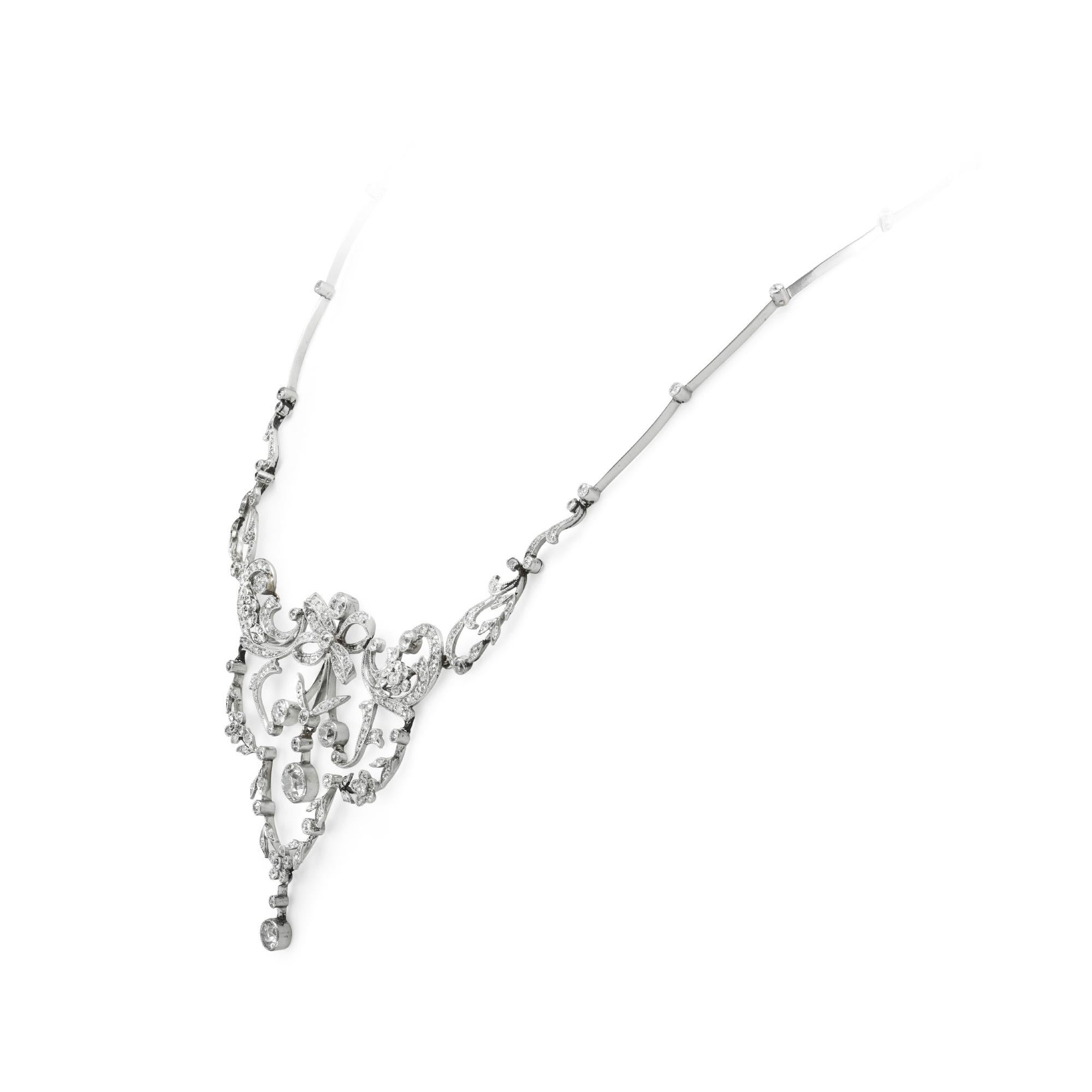 An Edwardian diamond necklace, the centre a diamond-set bow with diamond-set scroll, flower and foliate detail either side, suspending a garland of flowers and leaves surrounding an old round brilliant-cut diamond, all millegrain set, attached