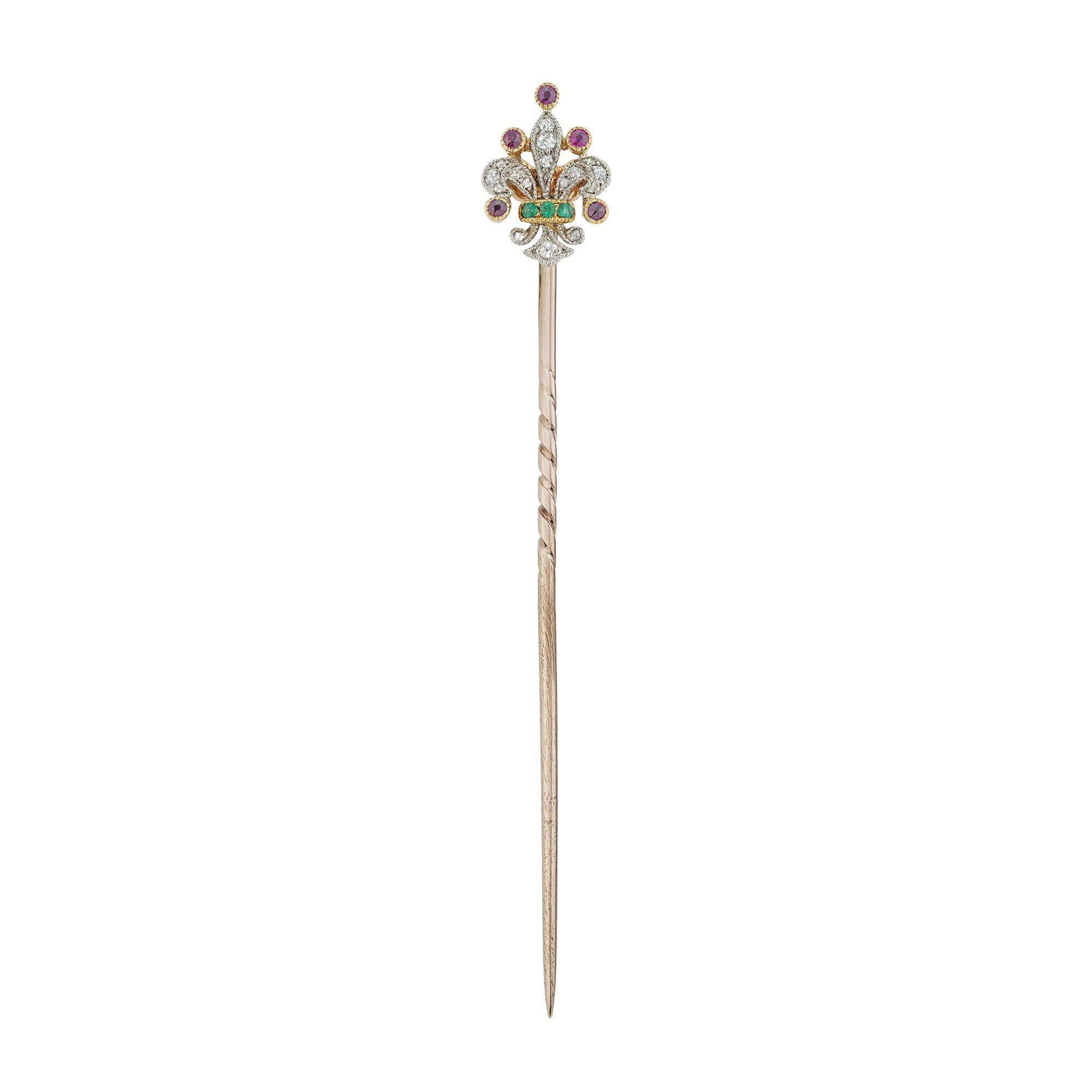 An Edwardian Fleur-de-lis gem-set stick-pin, set with old European and rose-cut diamonds estimated to weigh ¼ carat in total, embellished with three small round faceted emeralds and five small round faceted rubies, all millegrain-set in platinum and