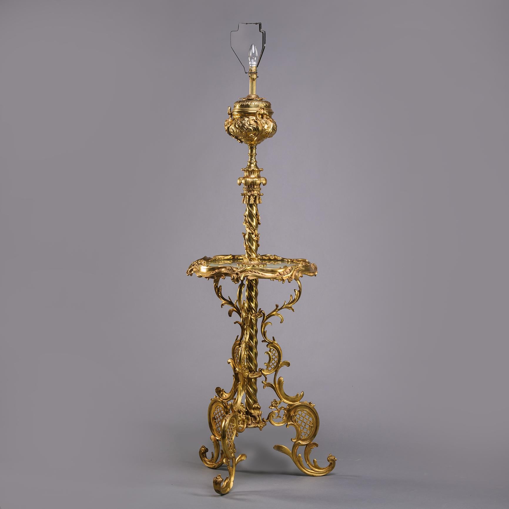 An Edwardian Gilt-Bronze Standard Lamp Tier Table.

Designed in the rococo style with spirally fluted stem supporting an urn with bulb fitment above. The central tier with green onyx top. Supporting on three 'C'-scroll legs.

England, Circa 1910.