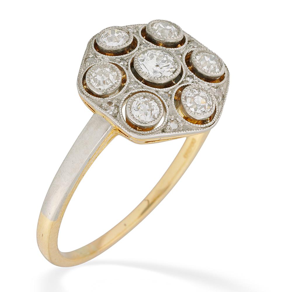 An Edwardian hexagonal shaped diamond panel ring, the seven old brilliant-cut diamonds estimated to weigh 0.8 carats in total, millegrain rubover-set to the centre of an open diamond-set cluster all set in platinum to an 18 carat yellow gold mount,
