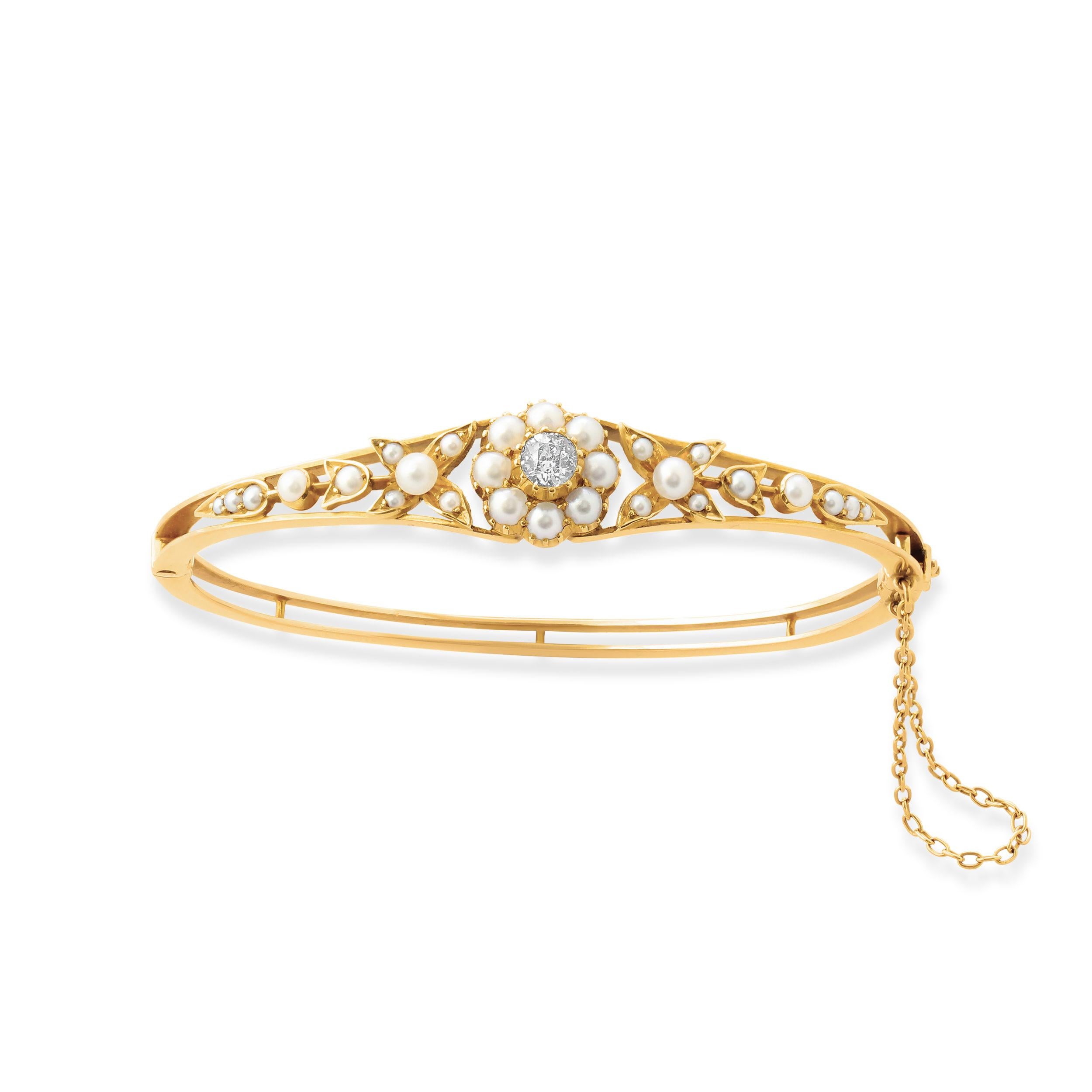 An Edwardian gold, diamond and pearl hinged bangle. Set at the centre with an old-cut diamond of approximately 0.35 carats surrounded by a cluster of natural pearls with additional pearls in a foliate design set along the front. 
