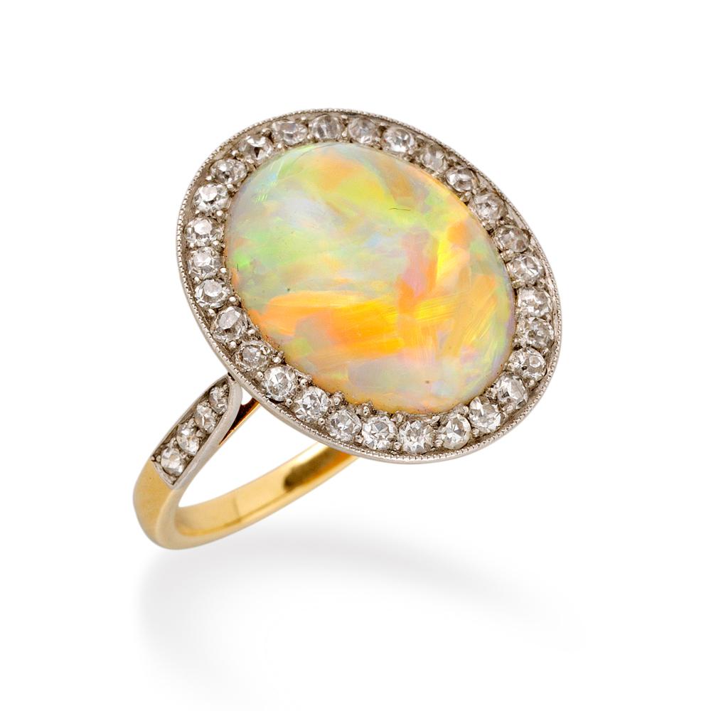 An Edwardian opal and diamond cluster ring, the oval cabochon opal weighing approximately 5.90 carats to the centre of an eight-cut diamond-set surround millegrain-set in platinum to an 18 carat yellow gold mount with diamond-set shoulders and