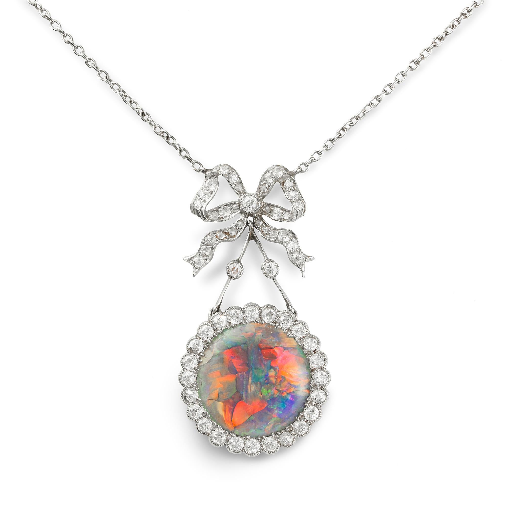 An Edwardian opal and diamond pendant, the central circular opal is surrounded by old brilliant-cut diamonds in a platinum millegrain setting suspended from a diamond-set bow attached to a white gold chain, circa 1910, the pendant measuring