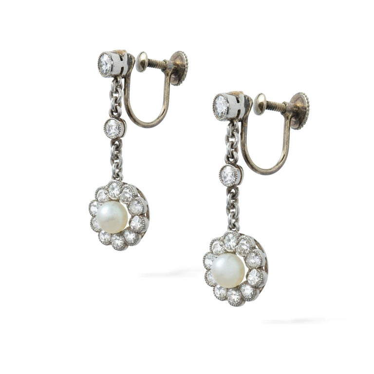 An Edwardian pair of pearl and diamond earrings, each earring consisting of a pearl, accompanied by GCS report stating to be natural saltwater, measuring approximately 4.5mm, surrounded by ten transition-cut diamonds, suspended by a chain set with
