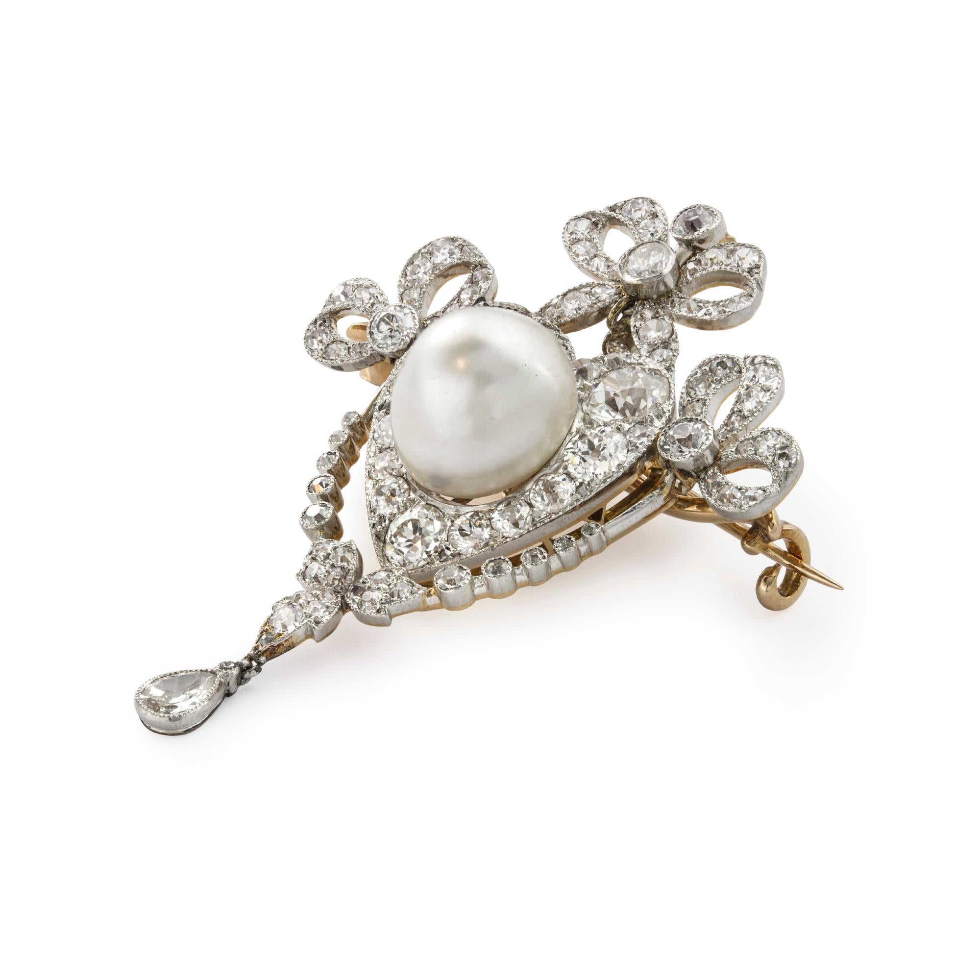 Eine edwardianische Perlen- und Diamantbrosche mit einer diamantbesetzten Schleifenfassung, die in der Mitte mit einer Perle in einem herzförmigen Cluster mit Diamanten im Altschliff besetzt ist. Die natürliche Perle misst etwa 10,1 x 9,6 mm.6 mm,
