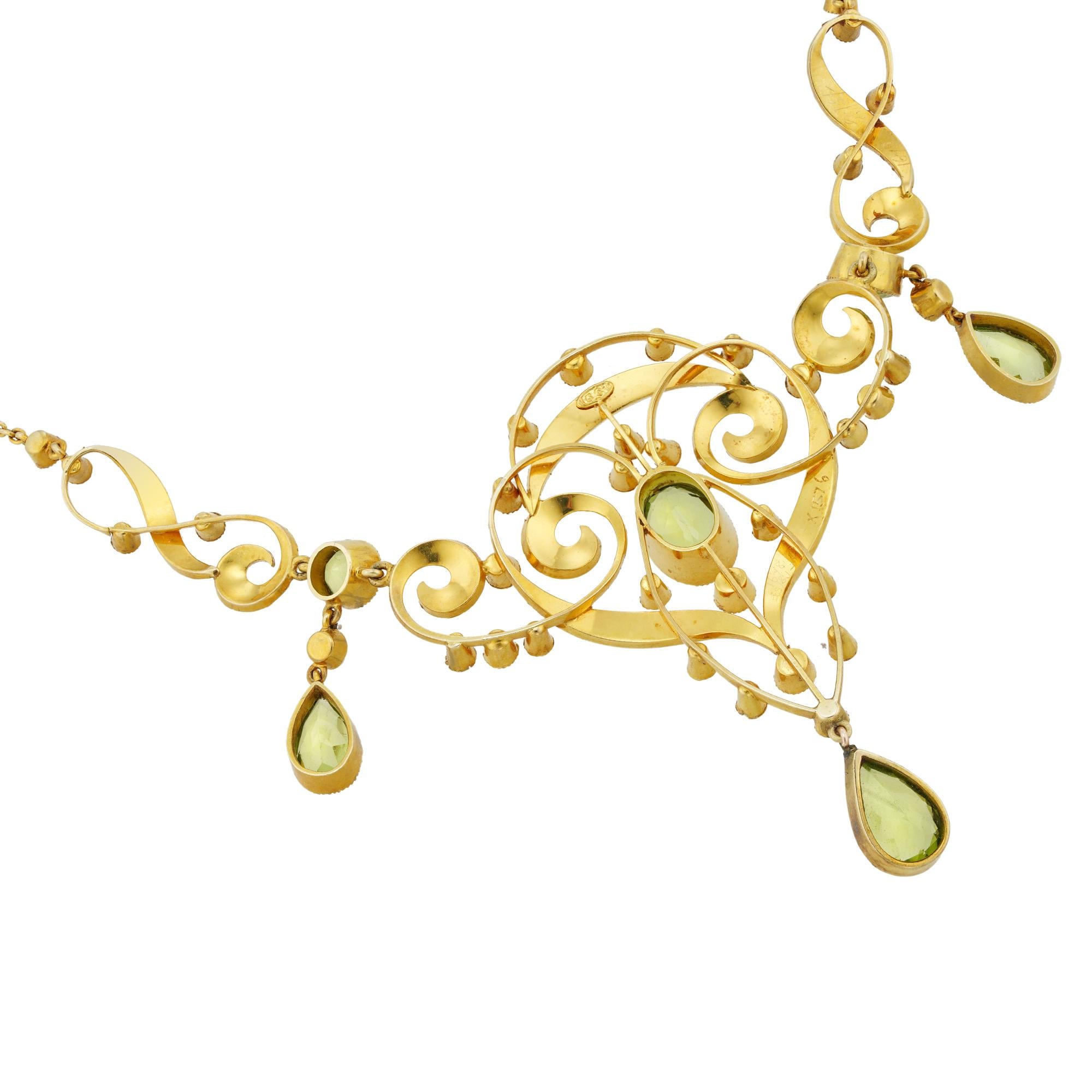 An Edwardian peridot and pearl necklace, to the centre an oval faceted peridot measuring 10x7mm millegrain-set to yellow gold collet, surrounded by gold openwork scroll-design frame embellished with small half pearls, and suspending a pear-shaped