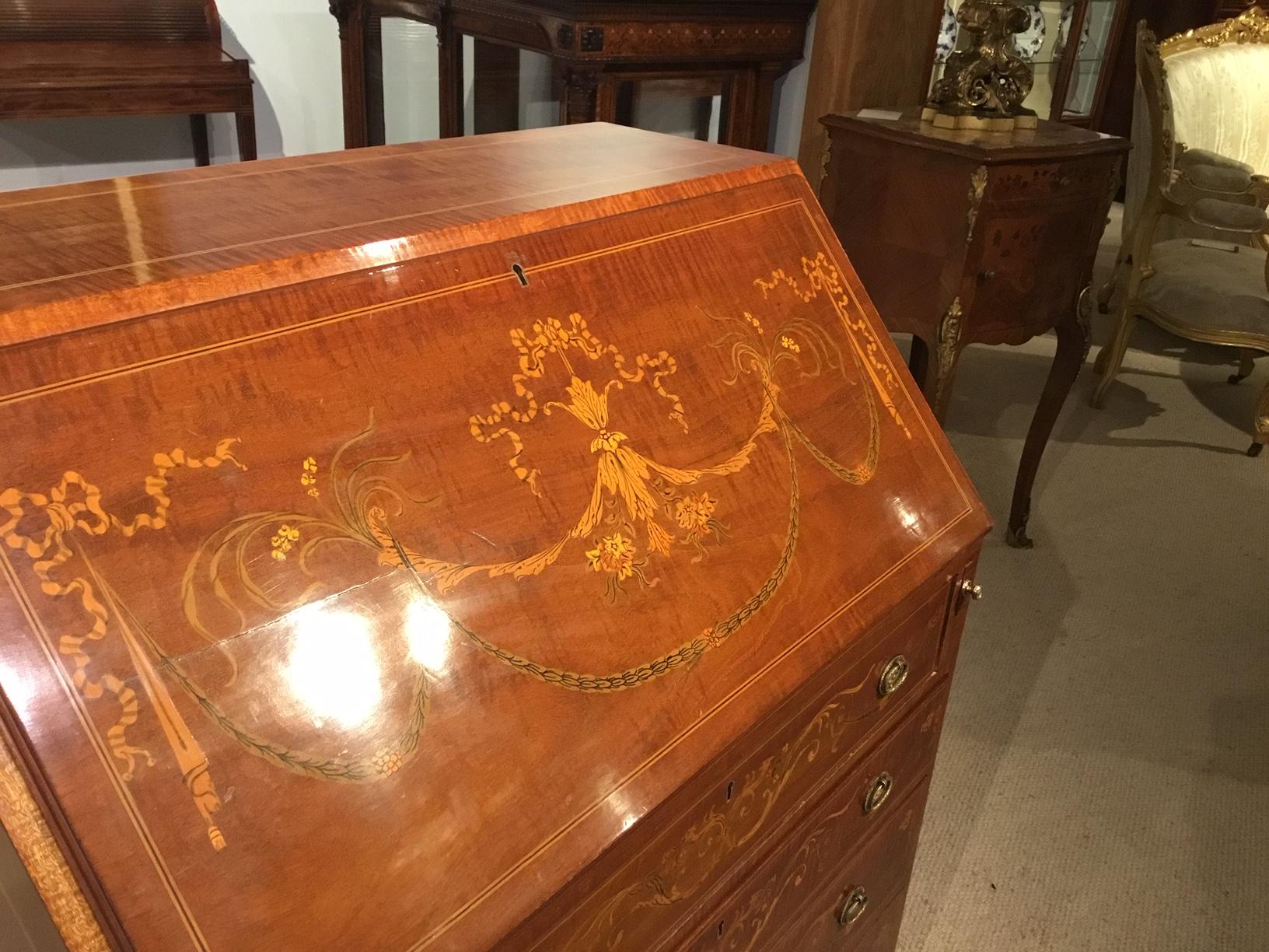 An Edwardian period mahogany inlaid antique bureau. Constructed using fiddleback mahogany and having a sloping fall front with fine marquetry and pen-work detail, opening to reveal a fitted interior with a green leather writing surface. The front