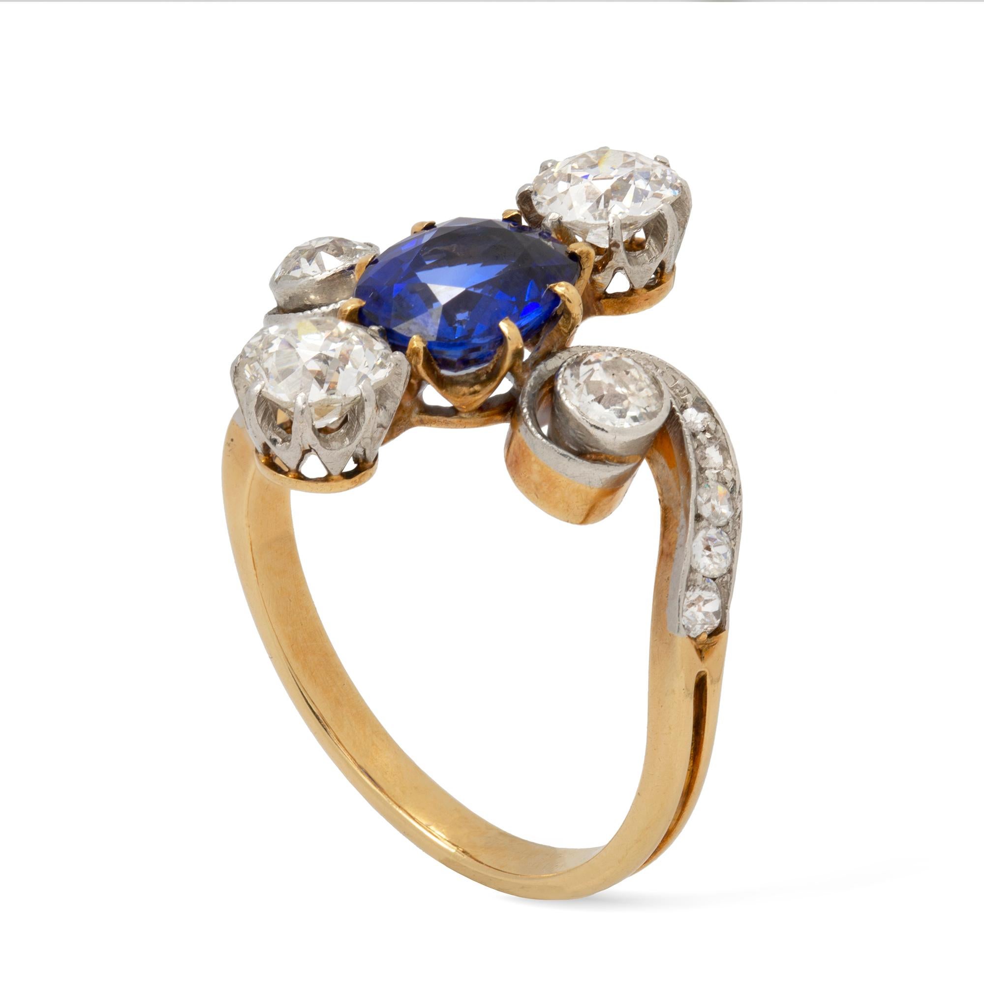 An Edwardian sapphire and diamond ring, the oval faceted sapphire estimated to weigh 1.2 carats, vertically set between two old-cut diamonds weighing approximately 0.50 carats each, to old-cut diamond-set scroll designed shoulders, all set in