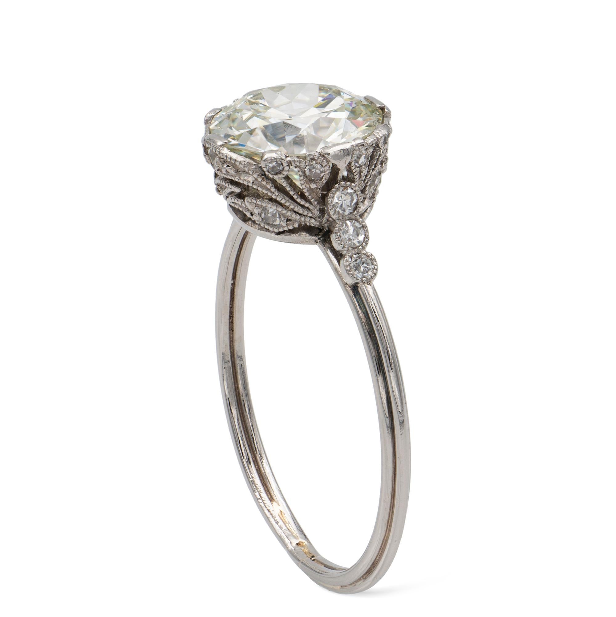 An Edwardian single-stone diamond ring, the old European-cut diamond weighing 1.95 carats, accompanied by GCS report stating to be of J colour and SI1 clarity, claw-set to an openwork collet of foliate design encrusted with small old-cut diamonds in