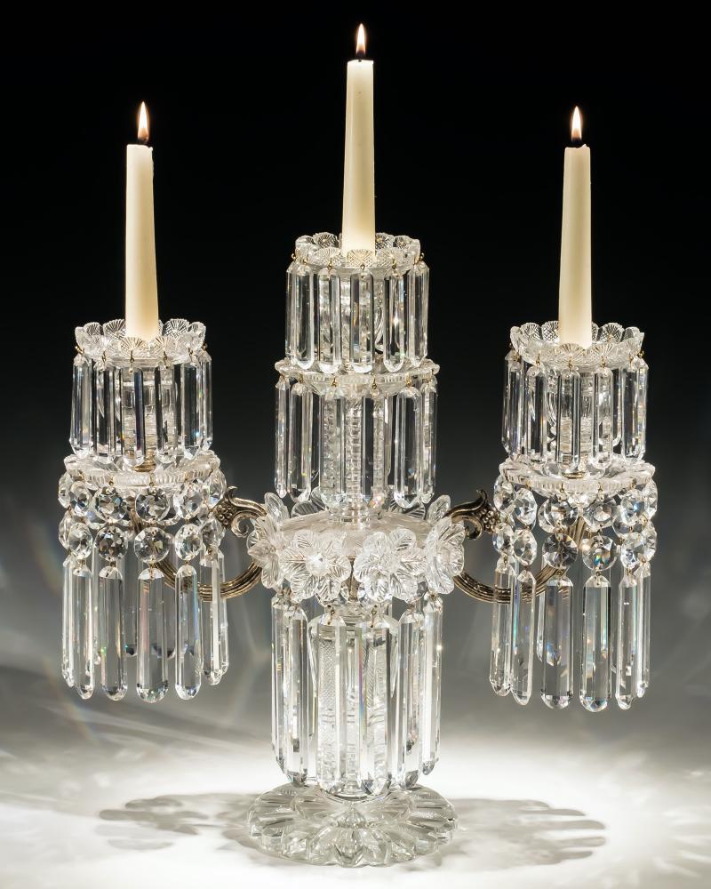 An elaborate three light candelabra with a pillar and file cut base mounted with a central silver band decorated with finely feather cut rosettes and hung with rounded rule drops surmounted by central light and two silver branches all with finely