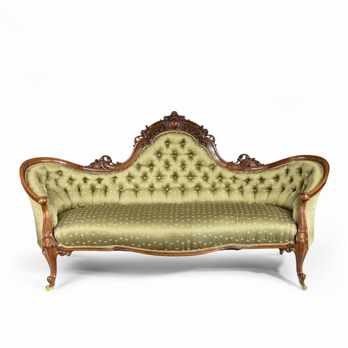 An elaborate Victorian shaped walnut sofa, the deep-buttoned back with an arched cresting rail and upswept corners curving down to scrolling arms continuing into cabriole legs with brass castors, with a serpentine seat rail, carved with a central