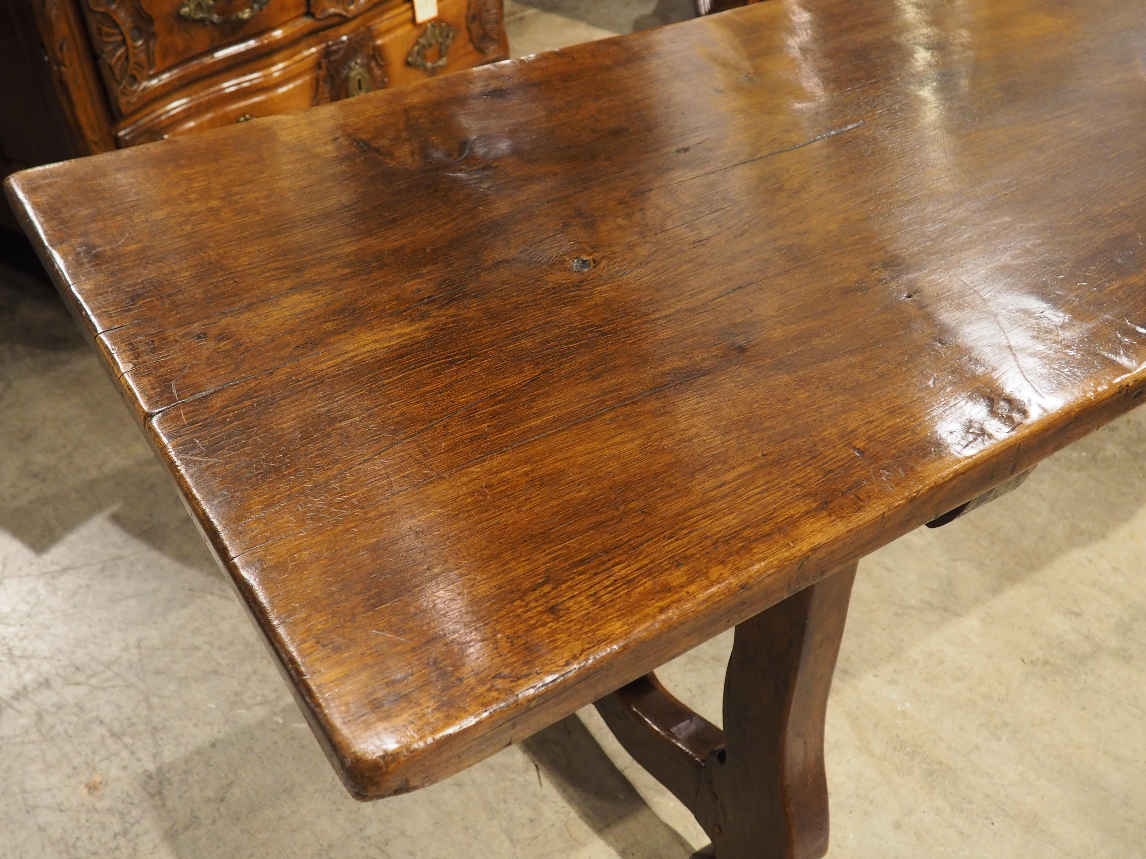 A beautiful example of a single plank table from Spain, this elegant walnut and oak dining table measures over nine feet long. Hand-carved in the 1700s, the table has been assembled true to the Spanish style: with a collapsible iron stretcher.