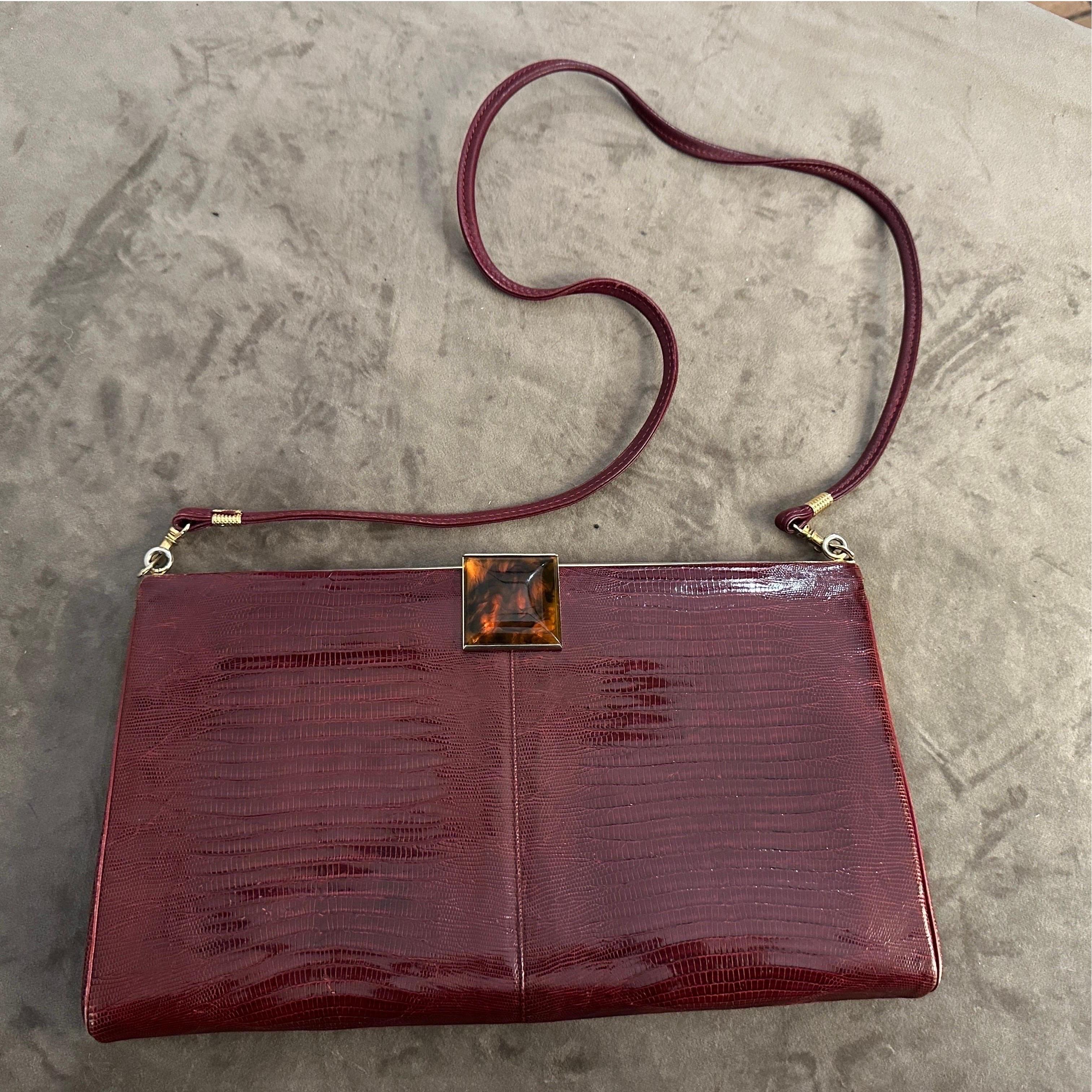 Diese elegante italienische Umhängetasche aus den 1950er Jahren strahlt mit ihrem burgunderroten Leder und der klassischen Eidechsenprägung zeitlose Raffinesse aus. Die Tasche hat eine schlichte, minimalistische Silhouette und ist mit einem