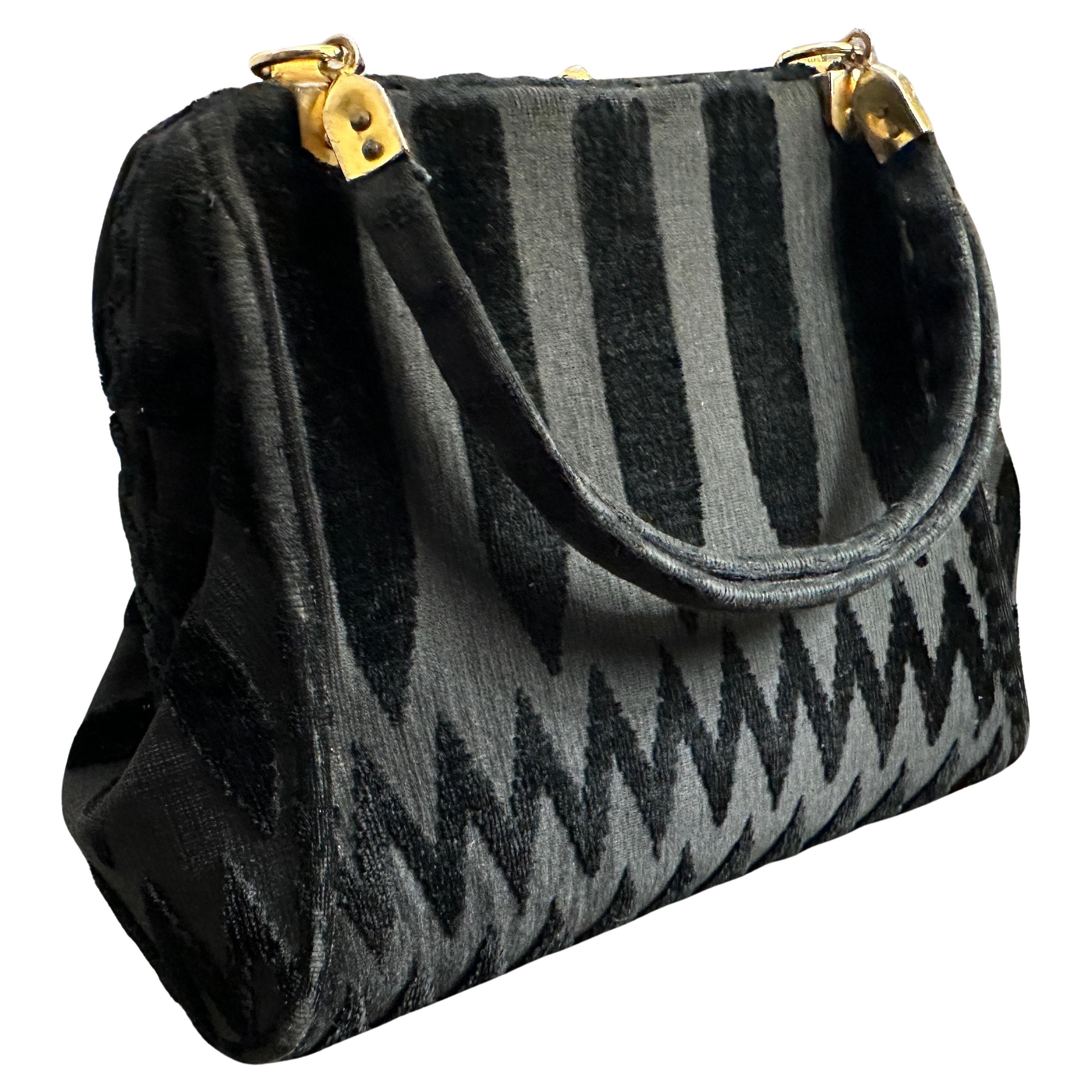 This 1970s black fabric handbag by Roberta di Camerino showcases the brand’s signature blend of luxurious materials, bold patterns, and timeless sophistication. The bag is crafted from plush black velvet fabric, a material often associated with